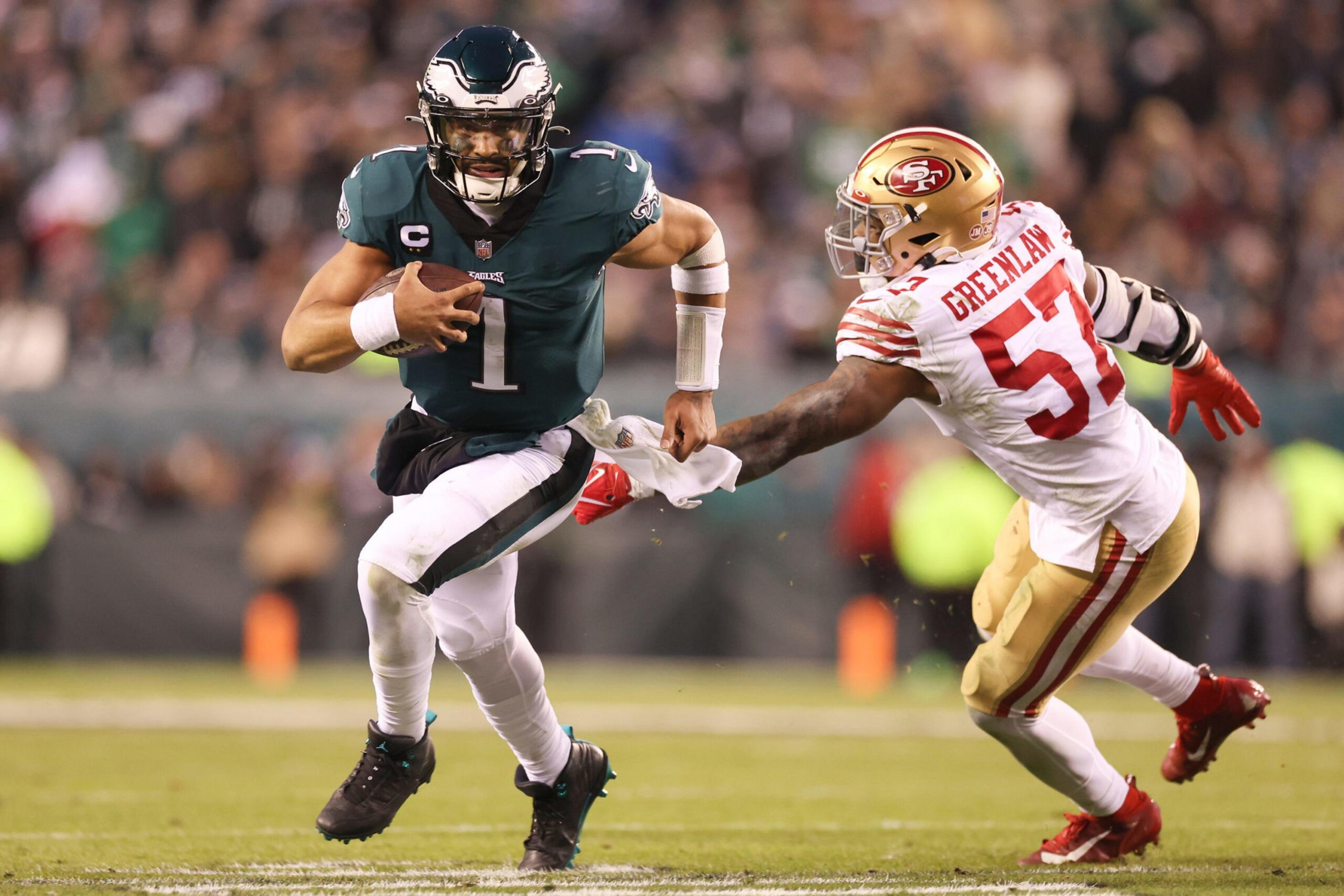 A football player in green runs with the ball while a player in white and gold tries to grab his jersey to stop him.