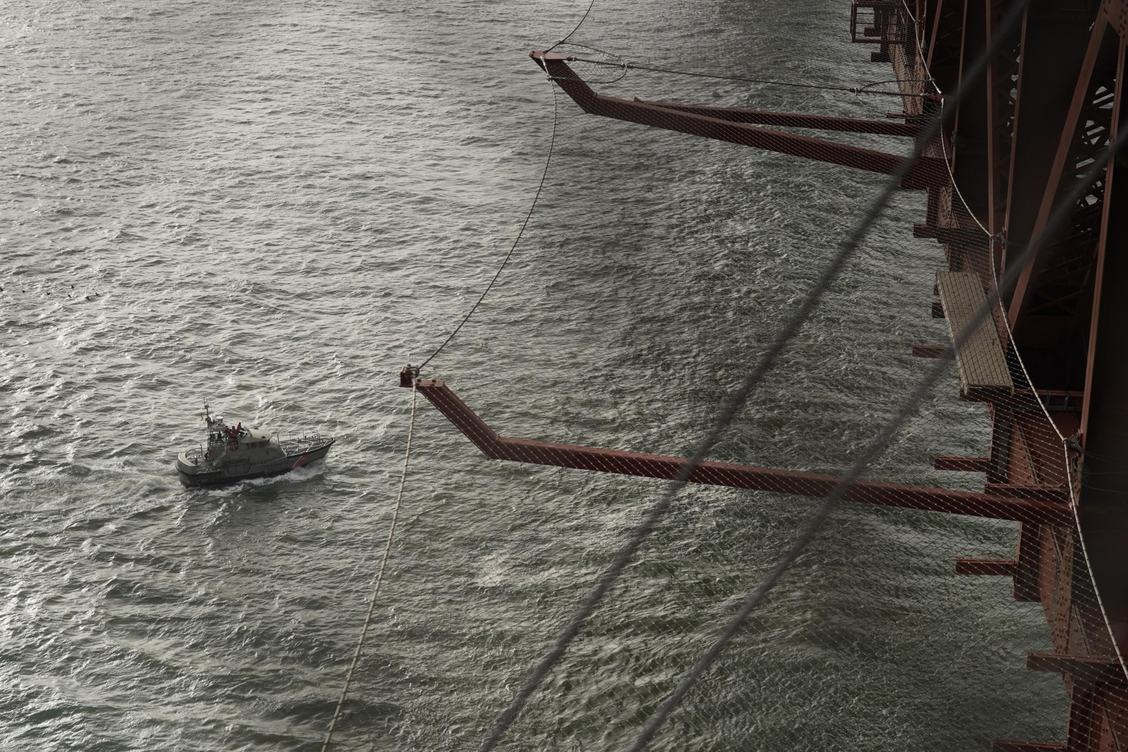 A ship passes below netting on side of red bridge