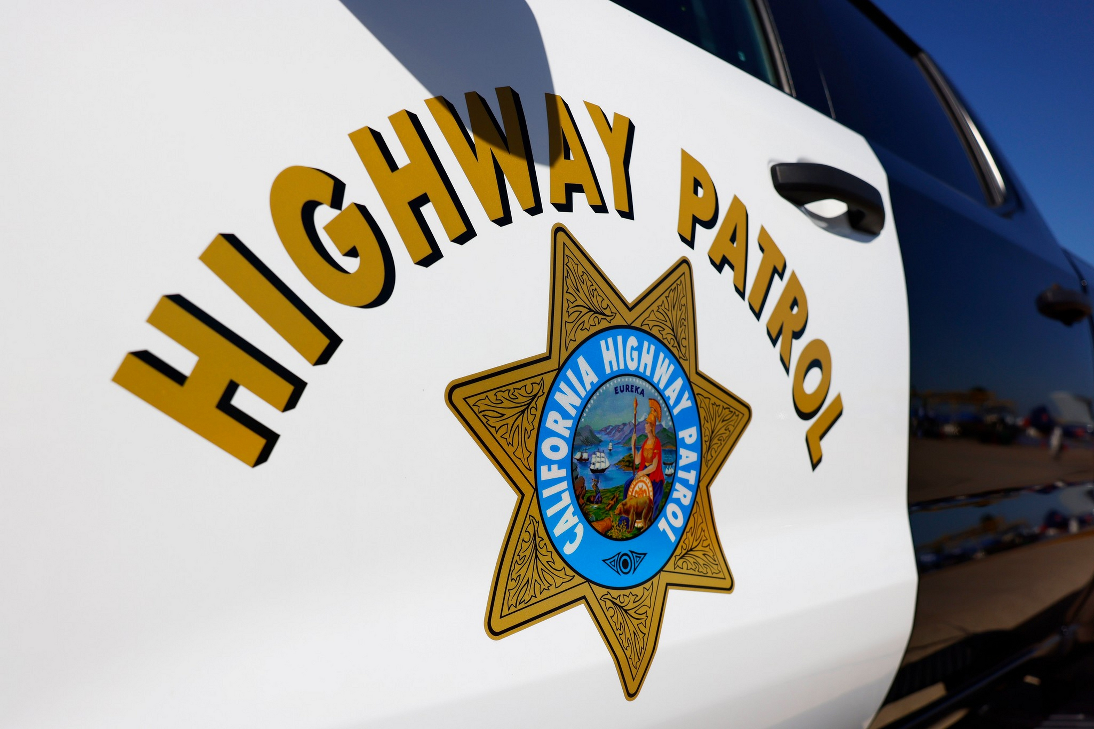 "Highway Patrol" is written above a gold seven-pointed star badge that reads "California Highway Patrol" on a black and white vehicle door.
