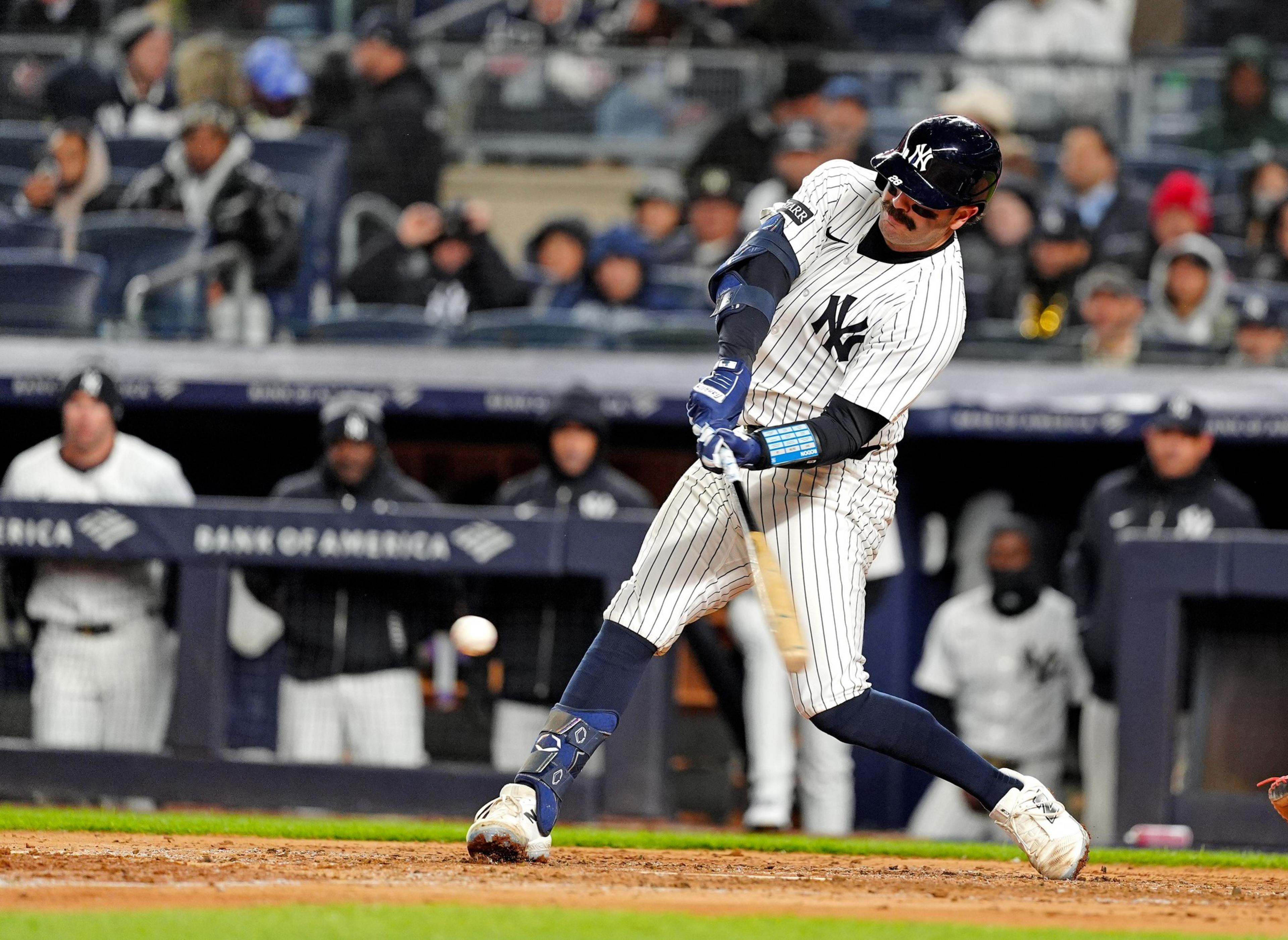 A baseball player in a pinstripe uniform swings at a pitch. He's mid-action with intense focus, while spectators watch from the stands.