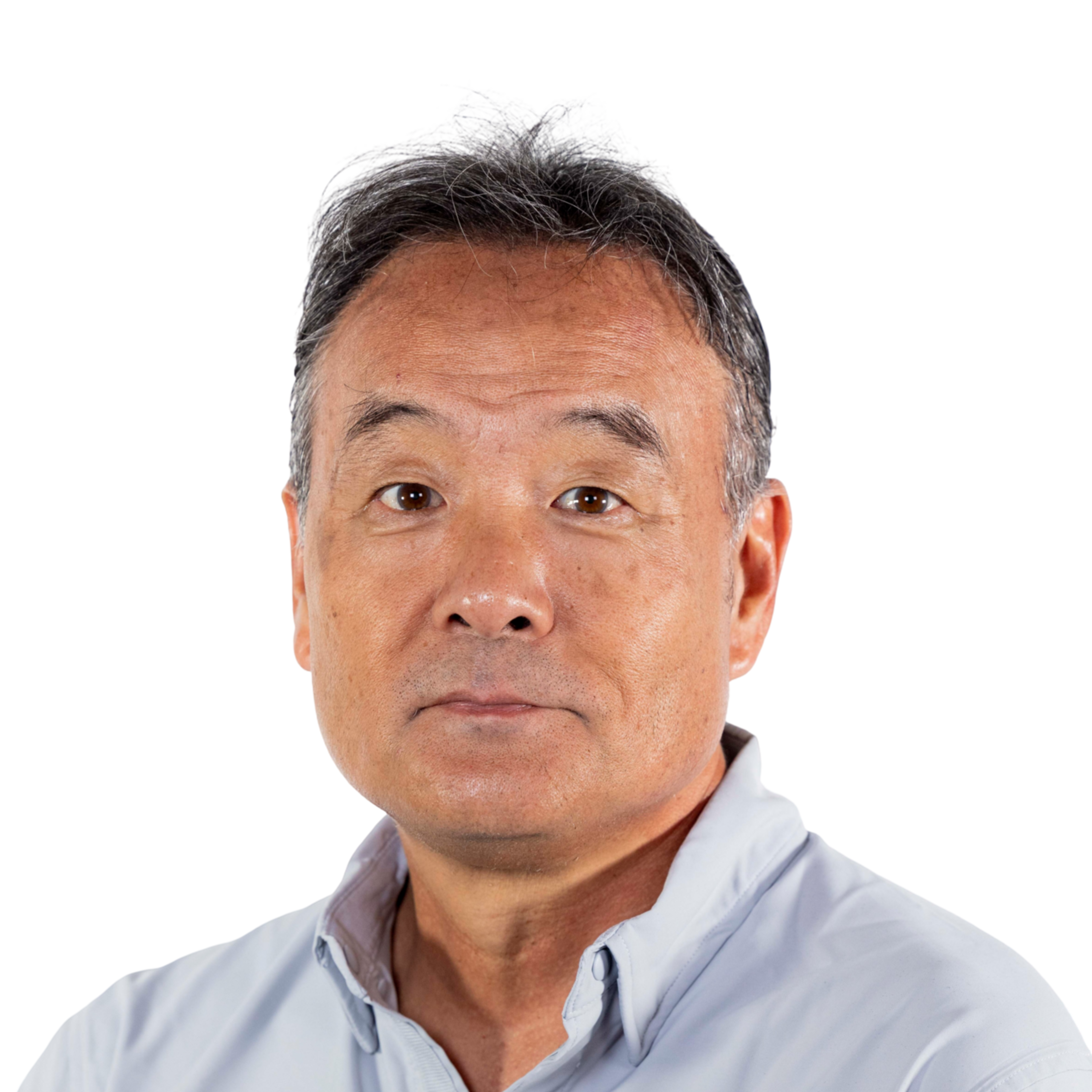 A middle-aged man with short, graying hair wears a light gray collared shirt and looks directly at the camera with a neutral expression.