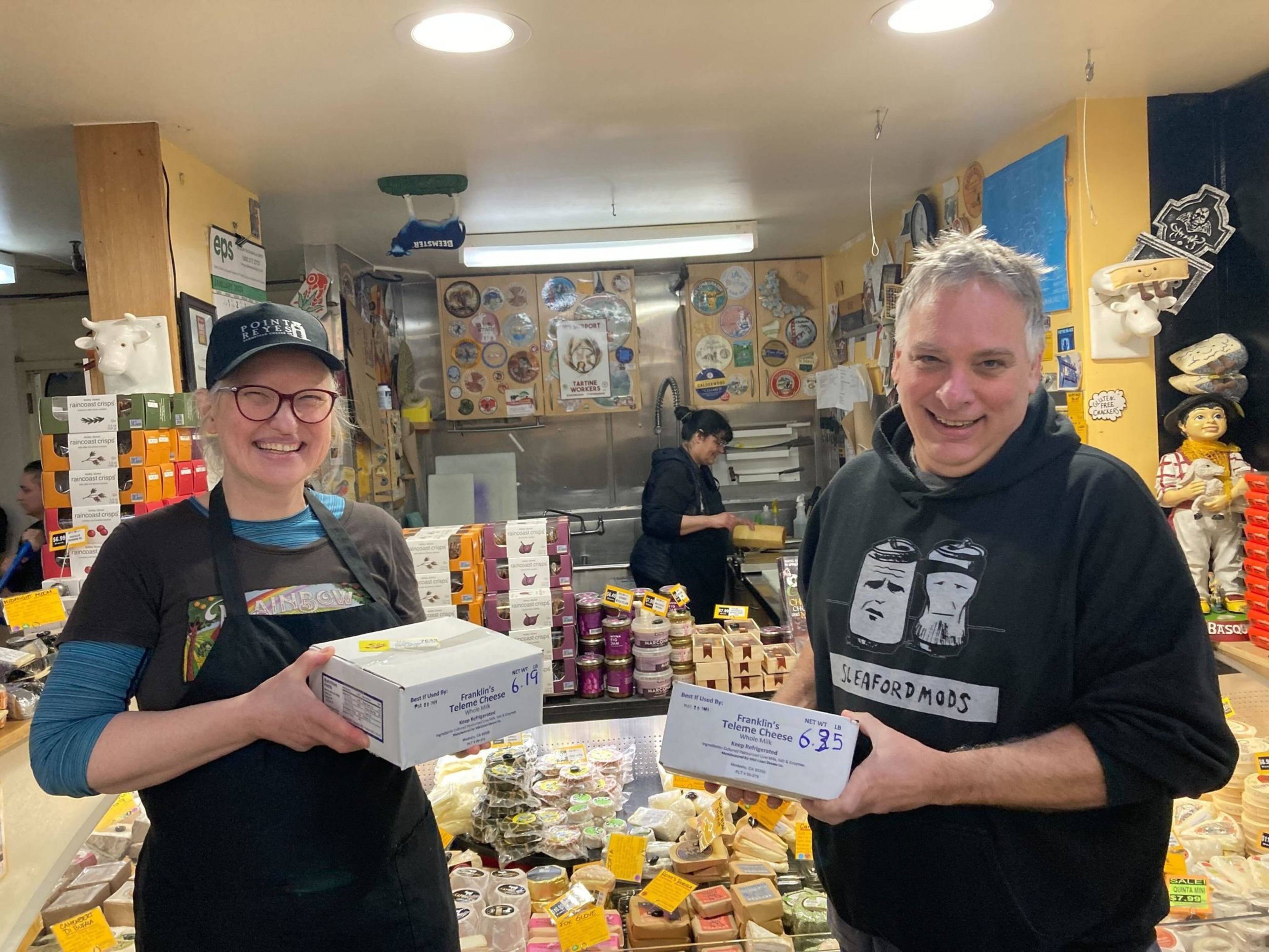 Two people hold boxes of cheese as they smile.