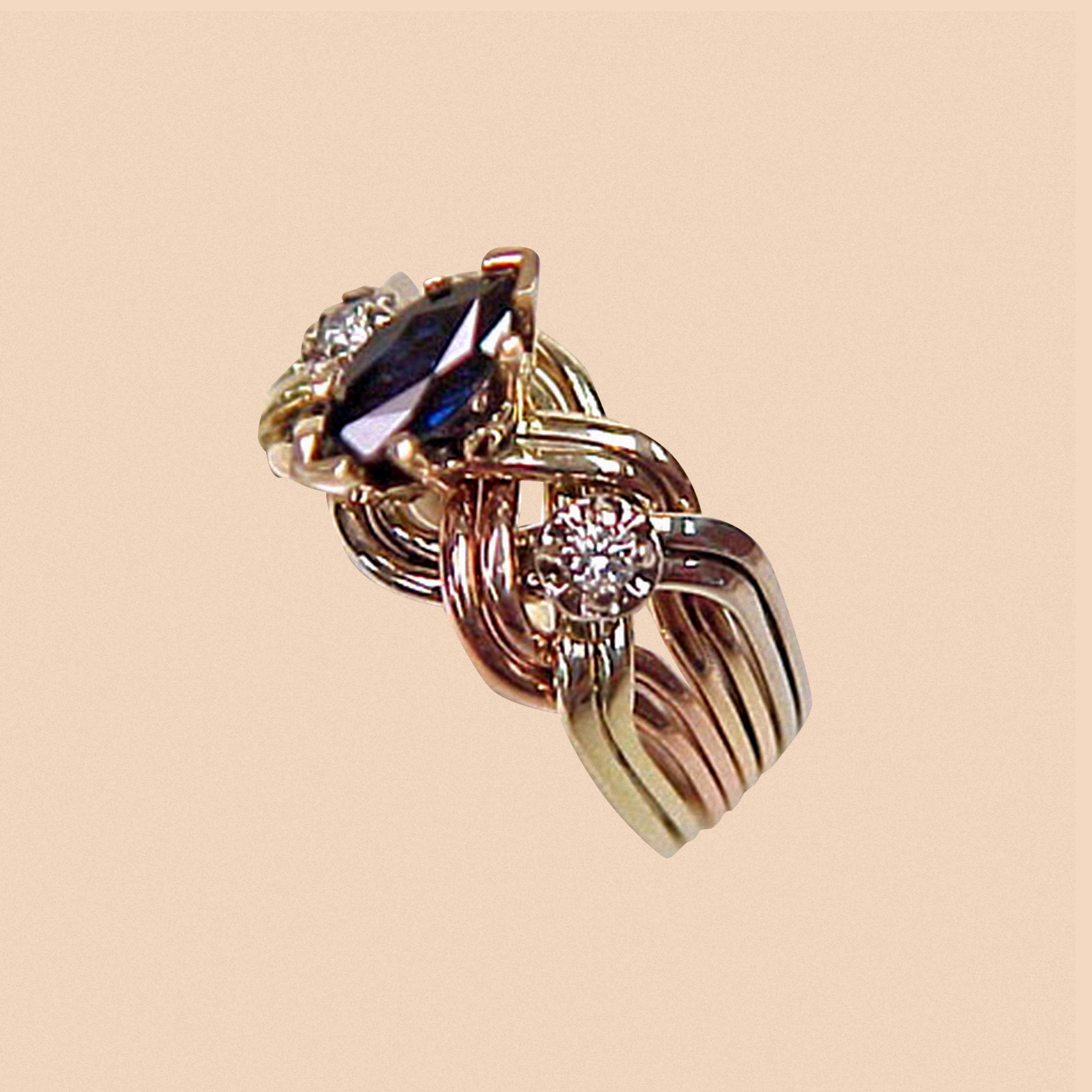 The image shows a ring with a twisted band design, featuring a central marquise blue gemstone flanked by two round clear stones.
