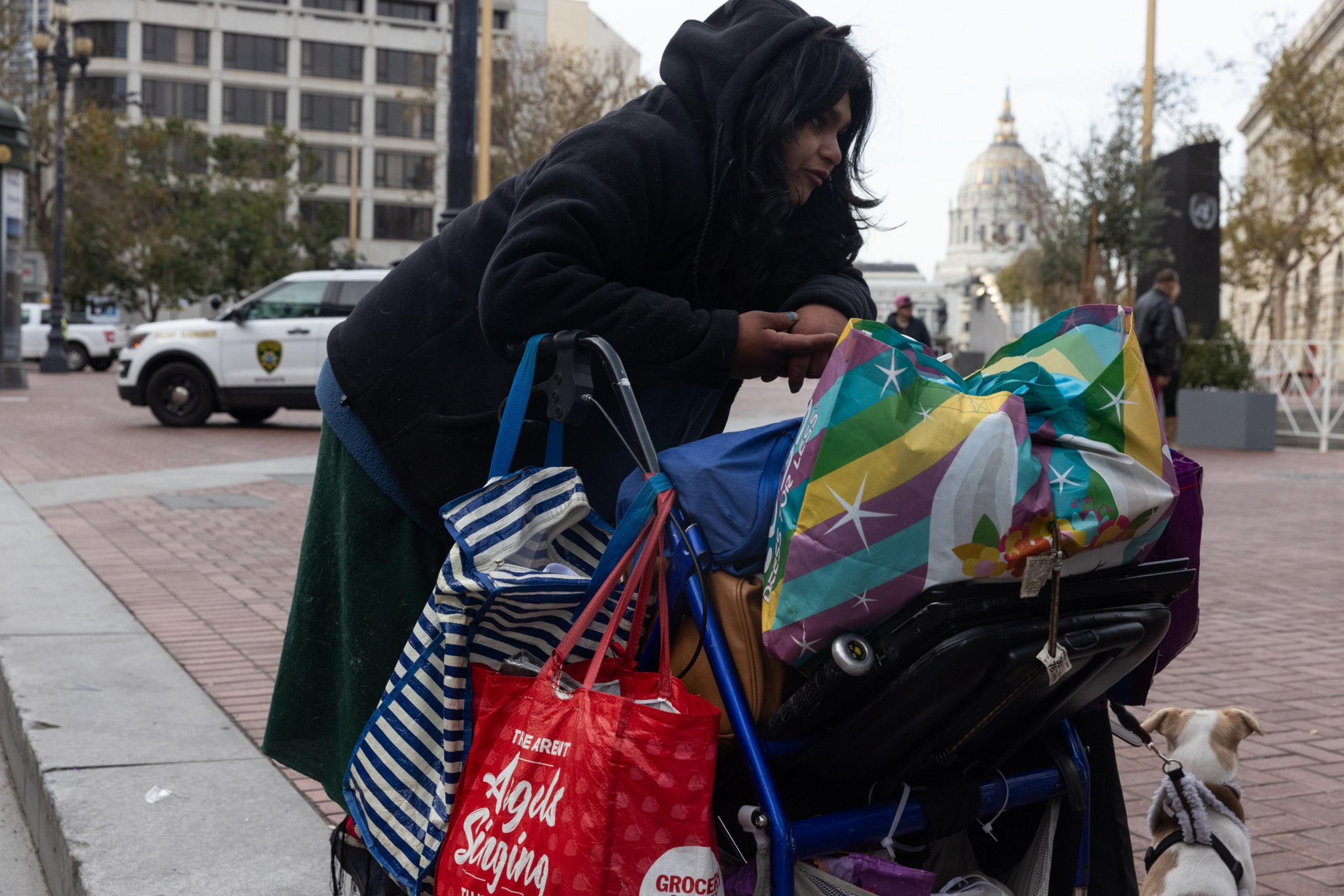 A women is hunched over her wheel chair with bags ontop of it.