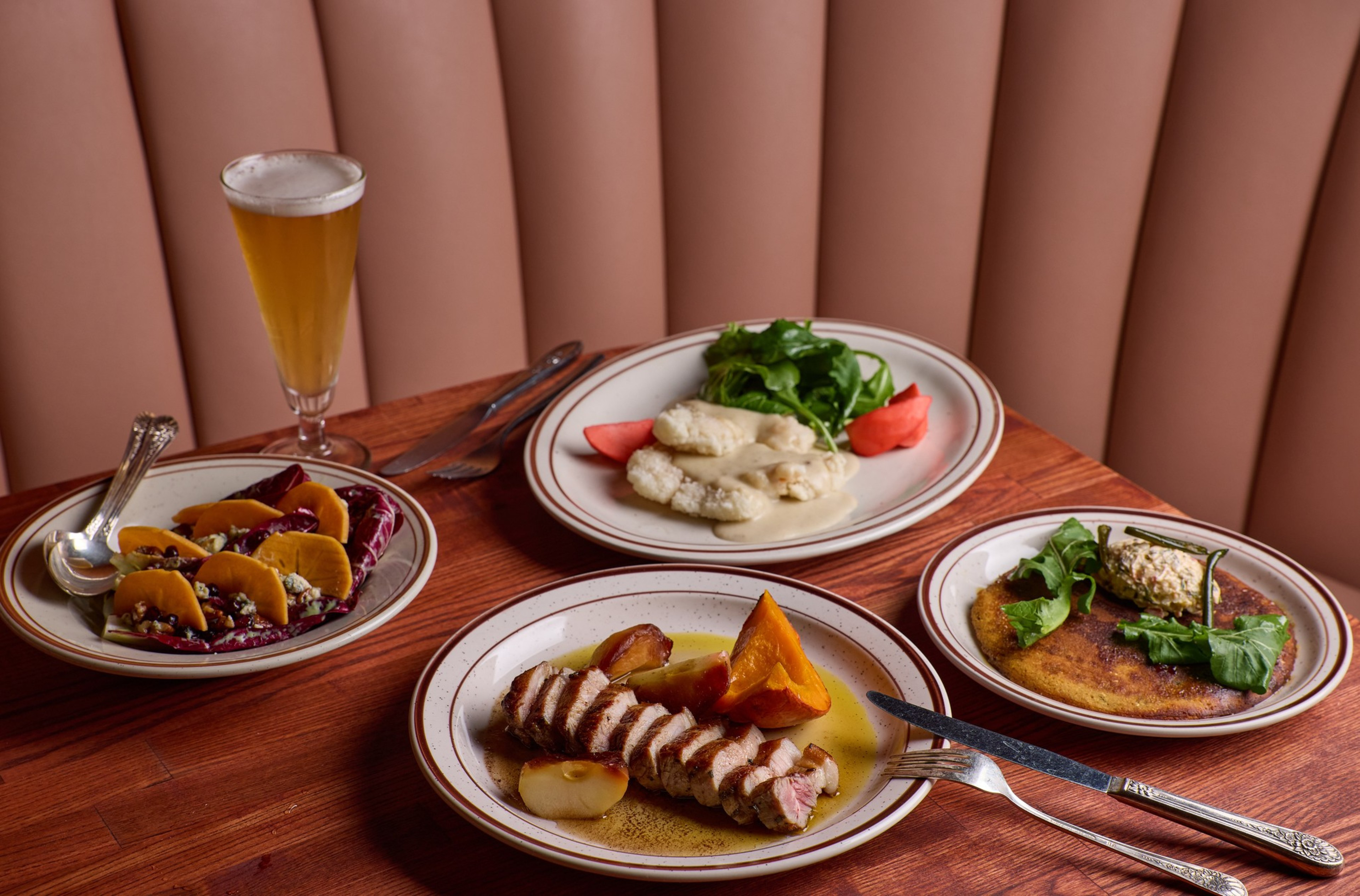 A meal with grilled meat and roasted vegetables, a fish fillet with greens and tomato, a salad with orange slices and nuts, a breaded patty with greens, and a glass of beer.