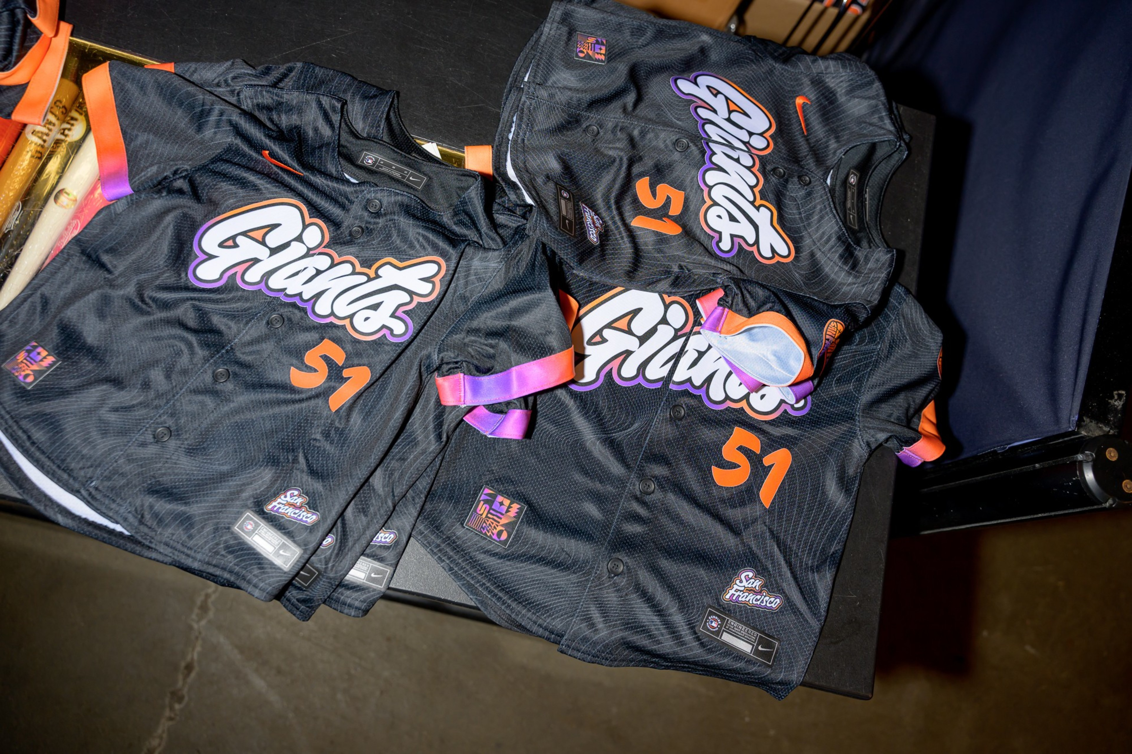 Three black baseball jerseys with &quot;Giants&quot; and number 51 in orange and white lettering are on a table, with purple and orange trim details.