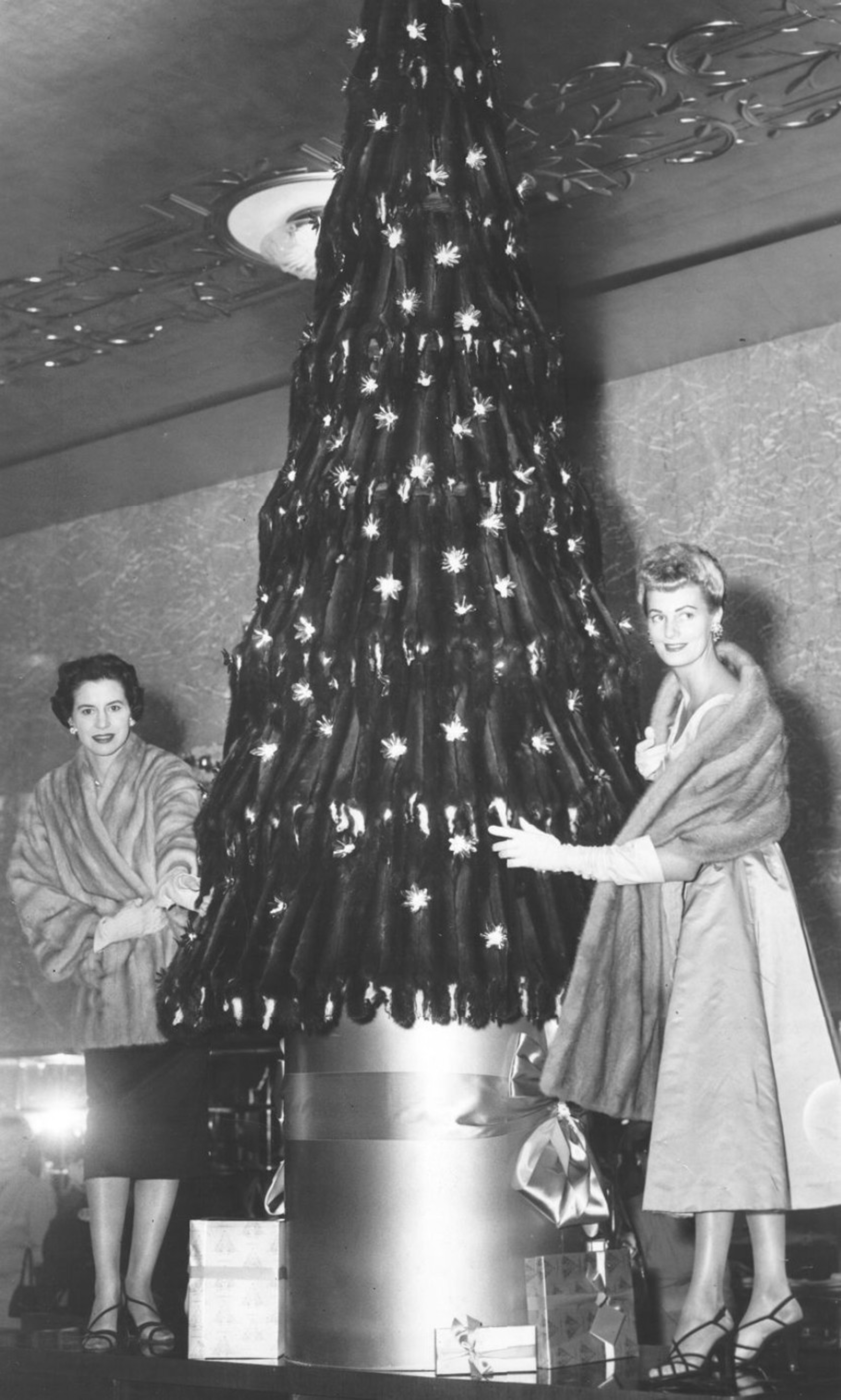 Two women stand next to a mink skin Christmas tree.