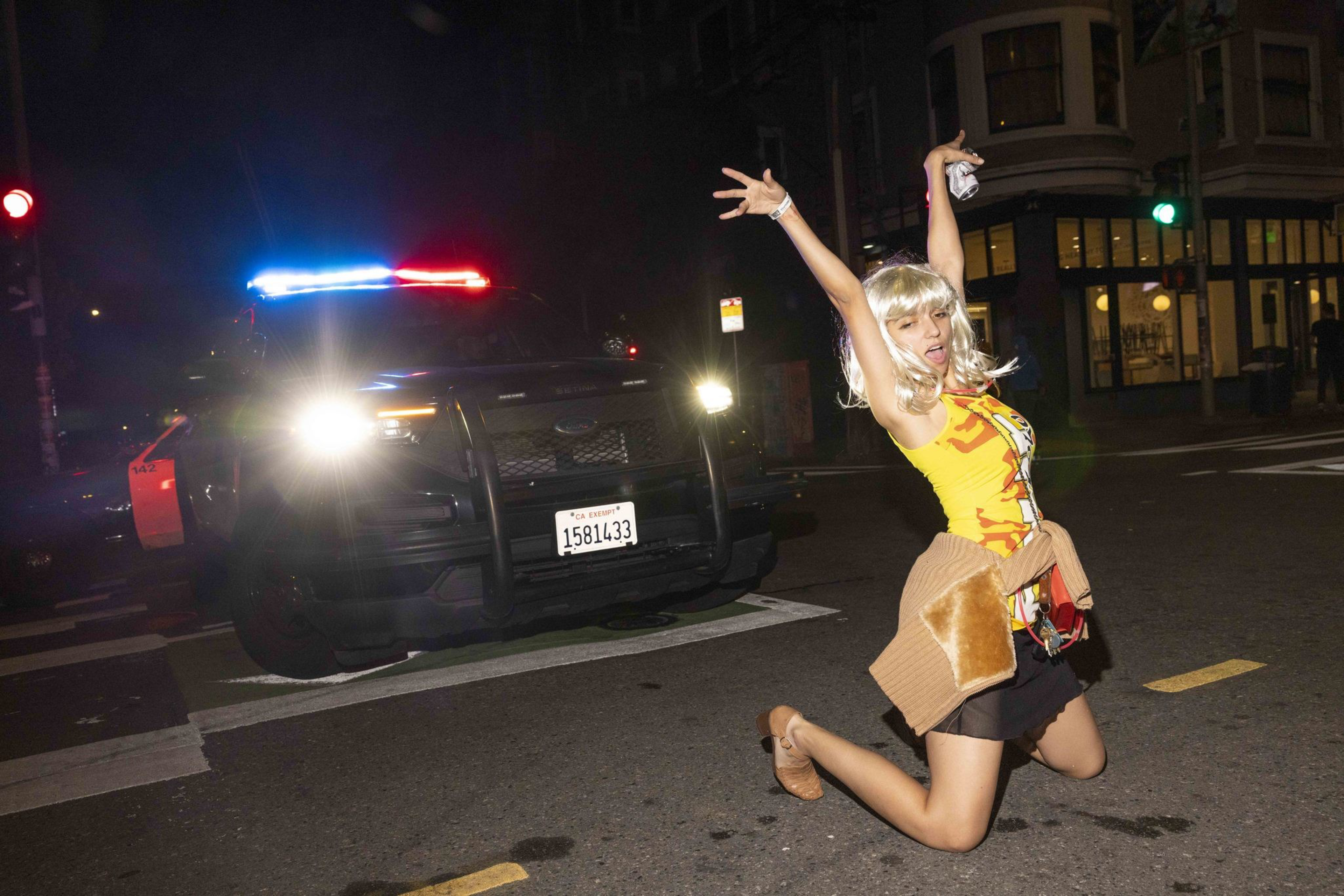 Marissa Lopez poses in front of a police car during a block party in the Mission in San Francisco on October 31, 2024. The party featured roaming deejays and shut down the area around 20th Street and Valencia.