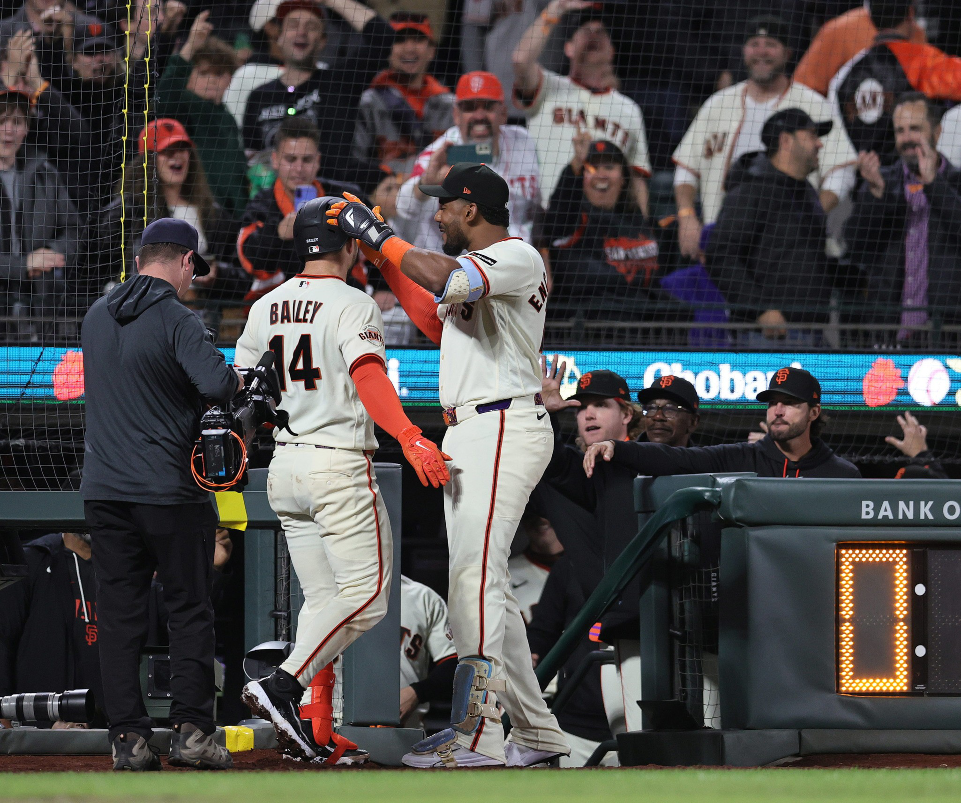 San Francisco Giants players celebrate a play near the dugout, with fans cheering behind the protective netting during a baseball game.