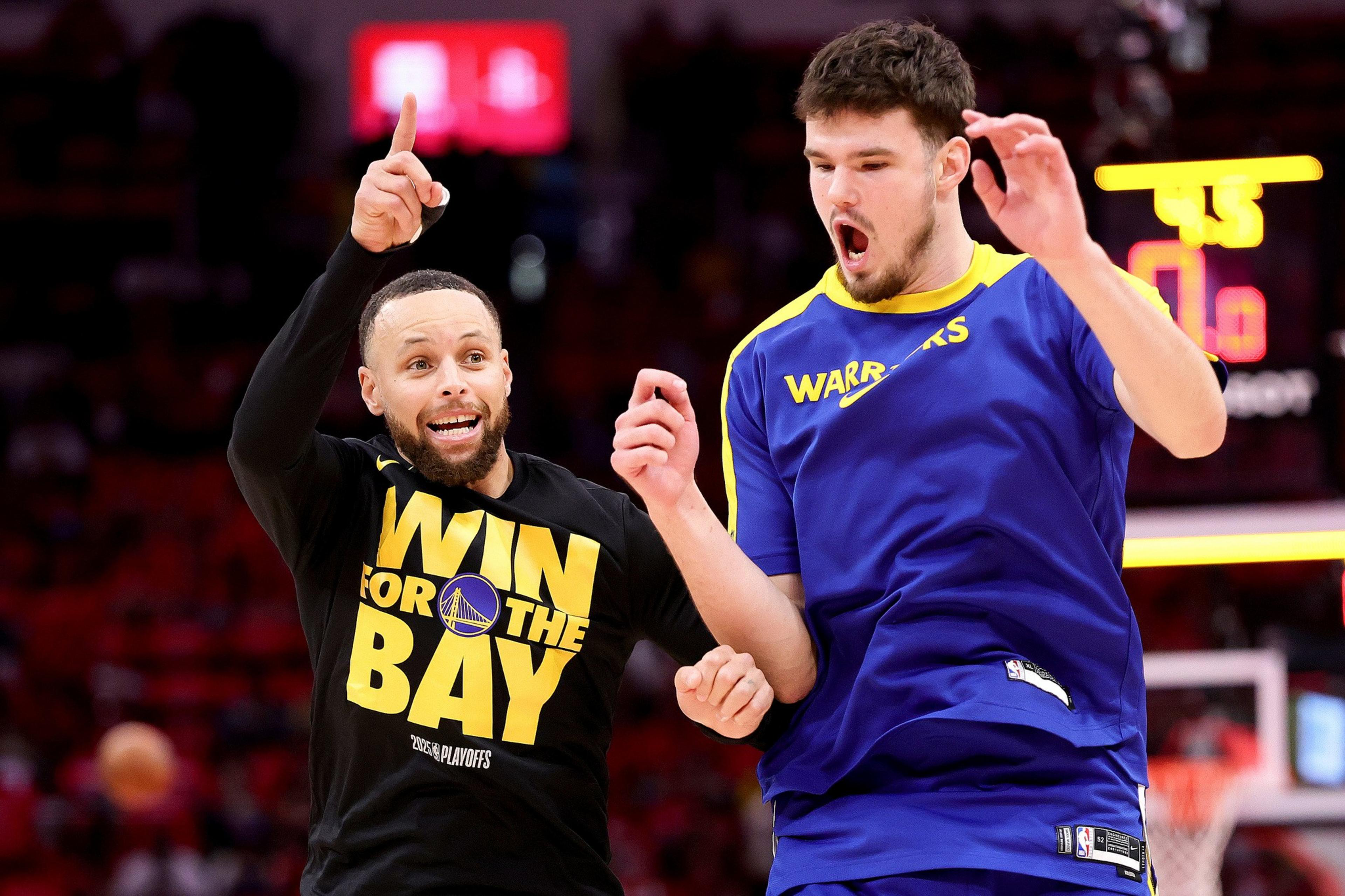 Two basketball players celebrate energetically. One wears a "Win for the Bay" shirt, pointing upwards, while the other in a Warriors jacket appears excited.