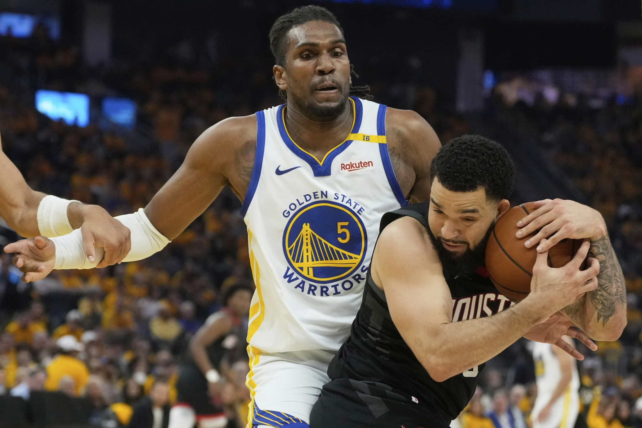 A basketball player in a white Golden State Warriors jersey defends against another player in a black Houston jersey who is holding the ball closely.