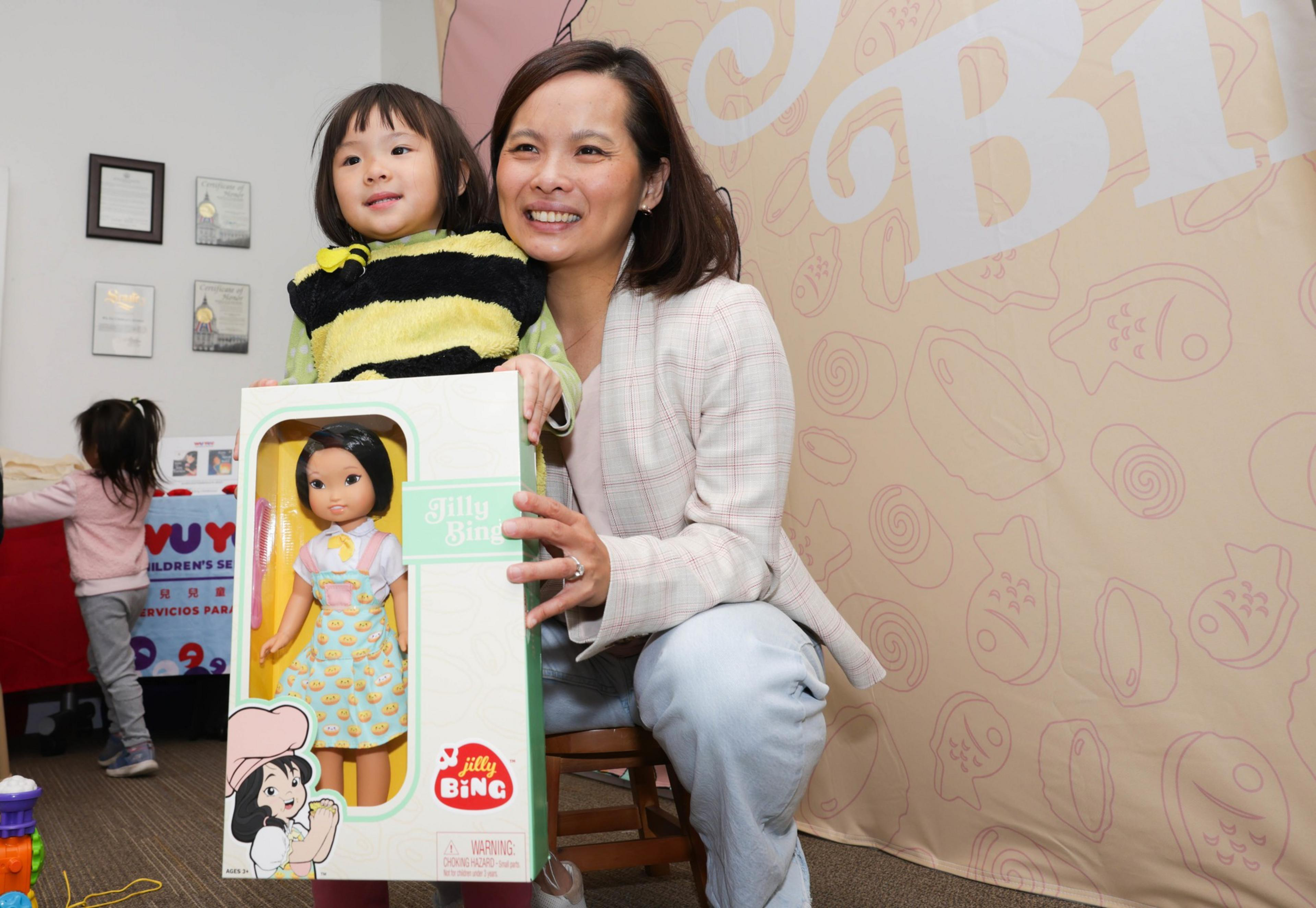 A kid embraced by their mom wile they pose for a picture while holding a doll.