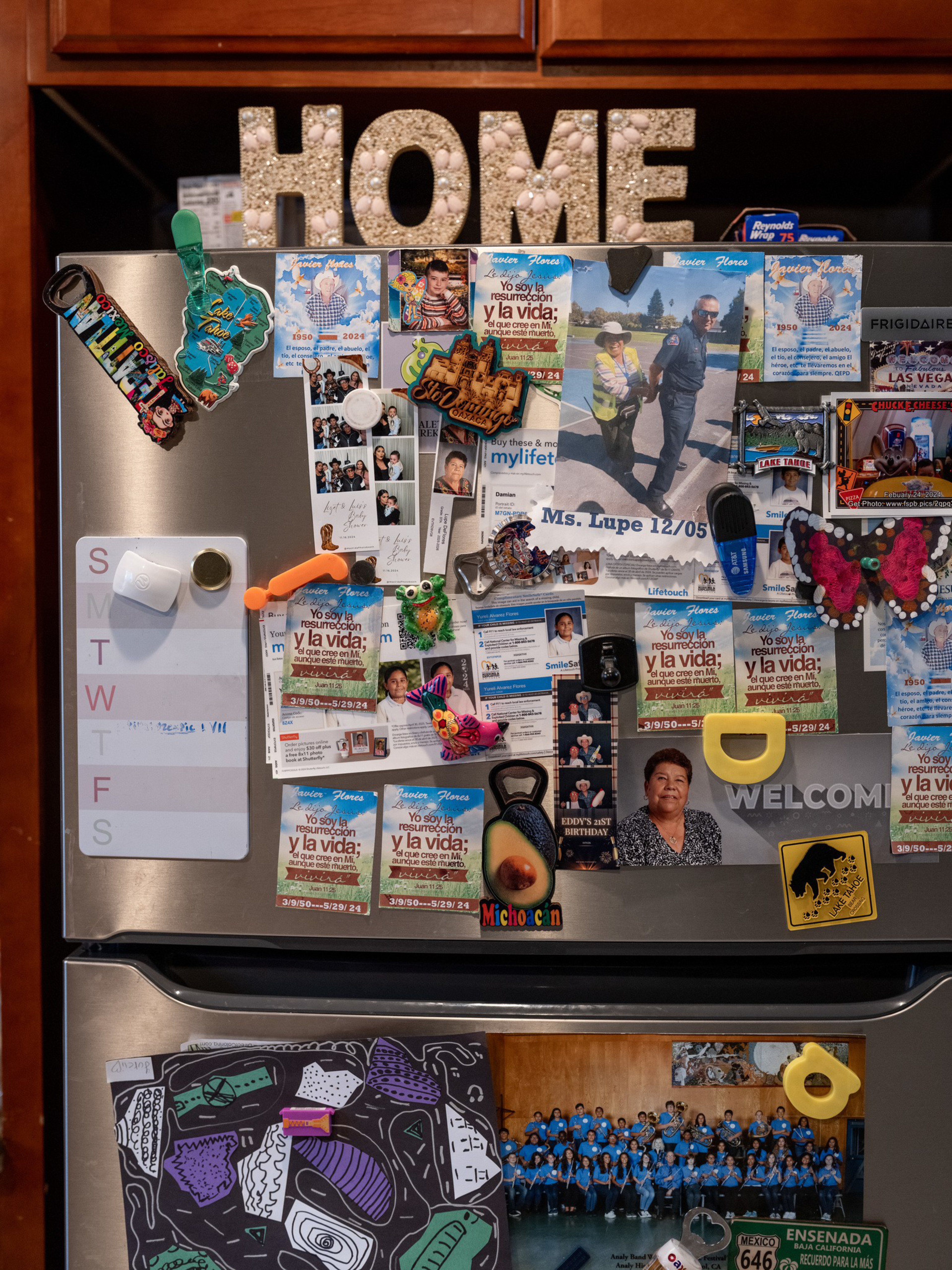 A refrigerator door covered with colorful magnets, photos, notes, and cards, including a large “HOME” sign embellished with shells on top.