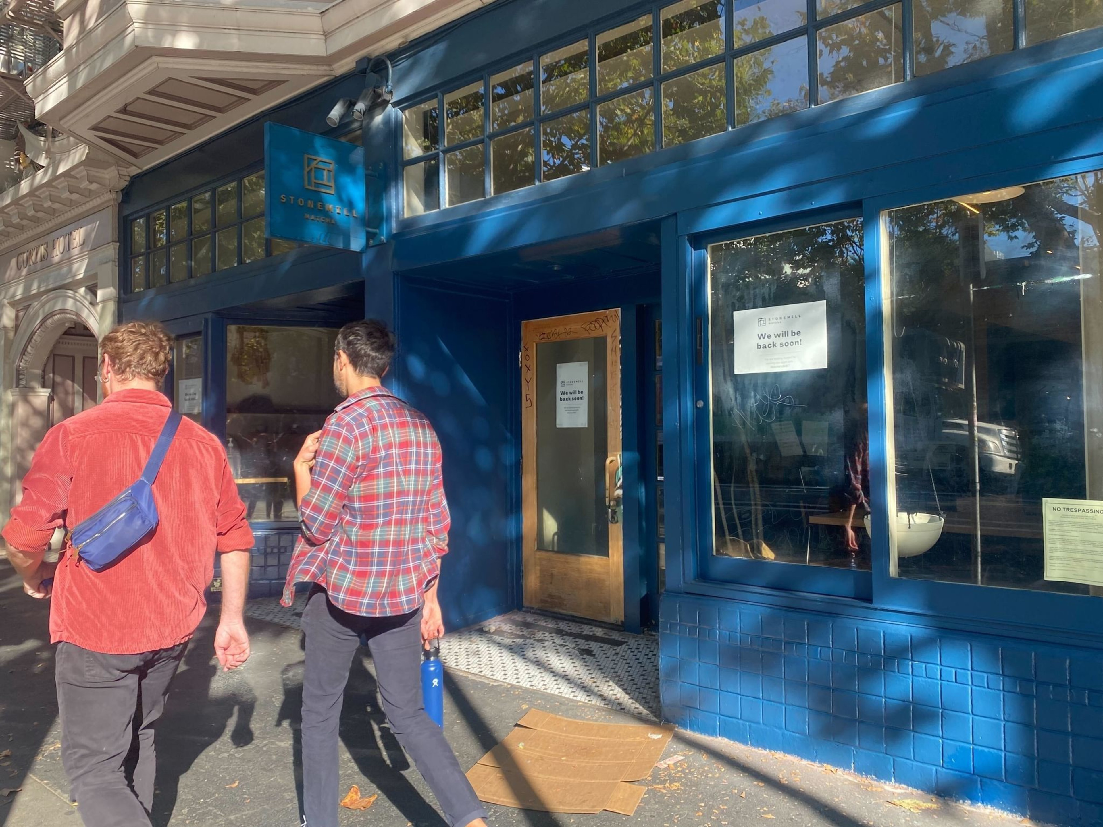 people walk past a coffee shop on the sidewalk
