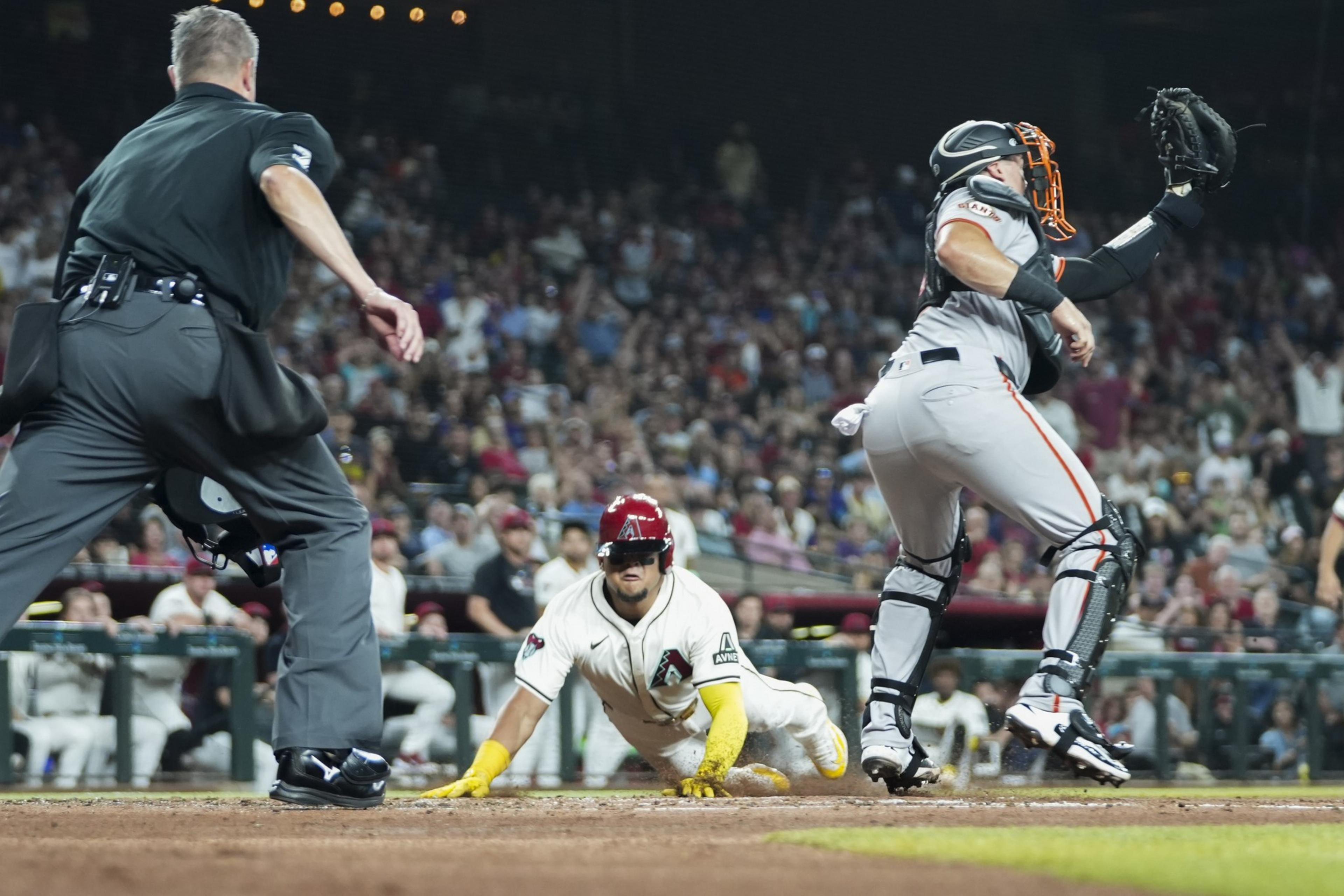 A baseball player slides head-first towards home plate as the catcher reaches up to catch the ball, with the umpire closely watching the play.