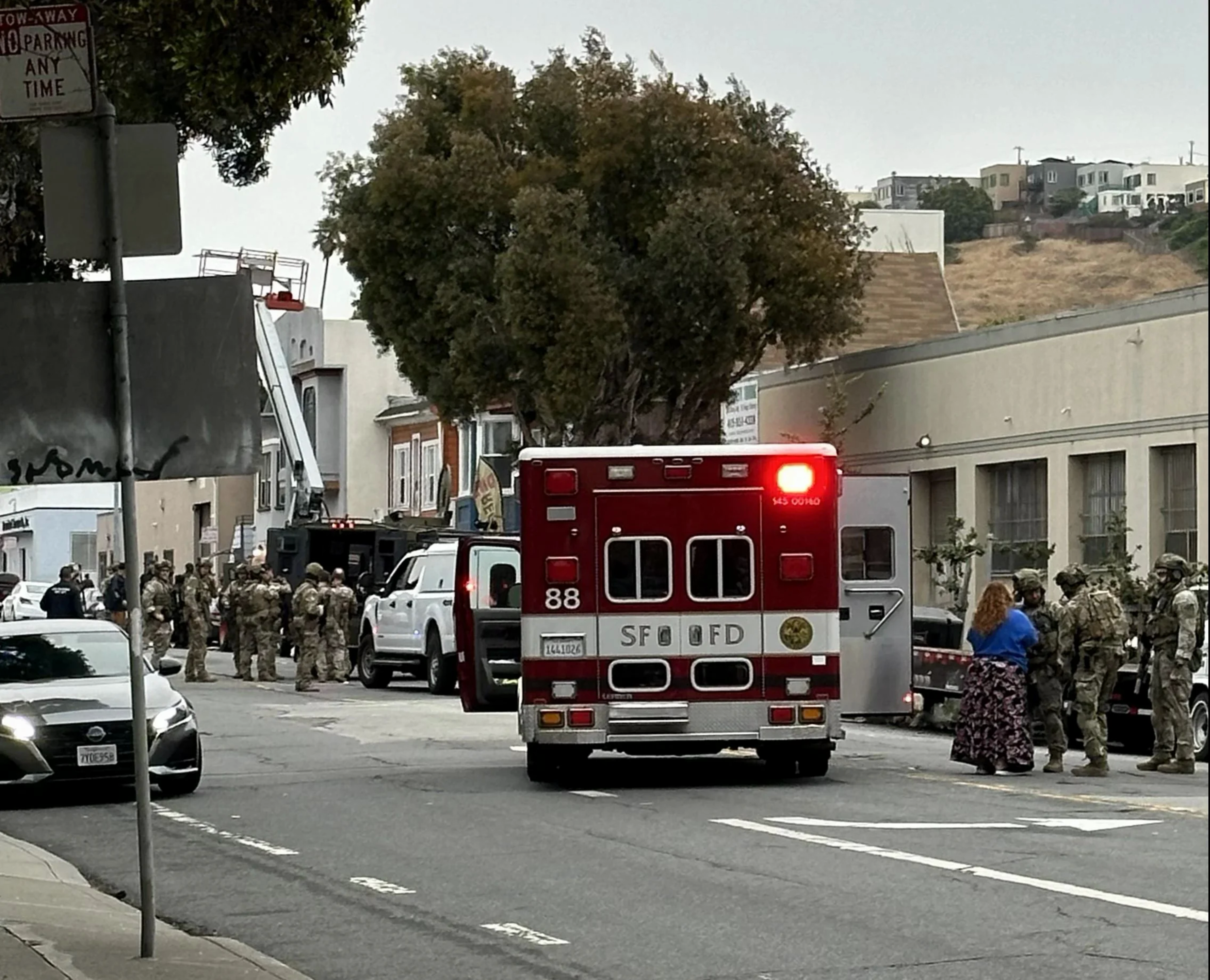 An ambulance with an open door is parked in the middle of a city street with uniformed law enforcement along both sides of it.