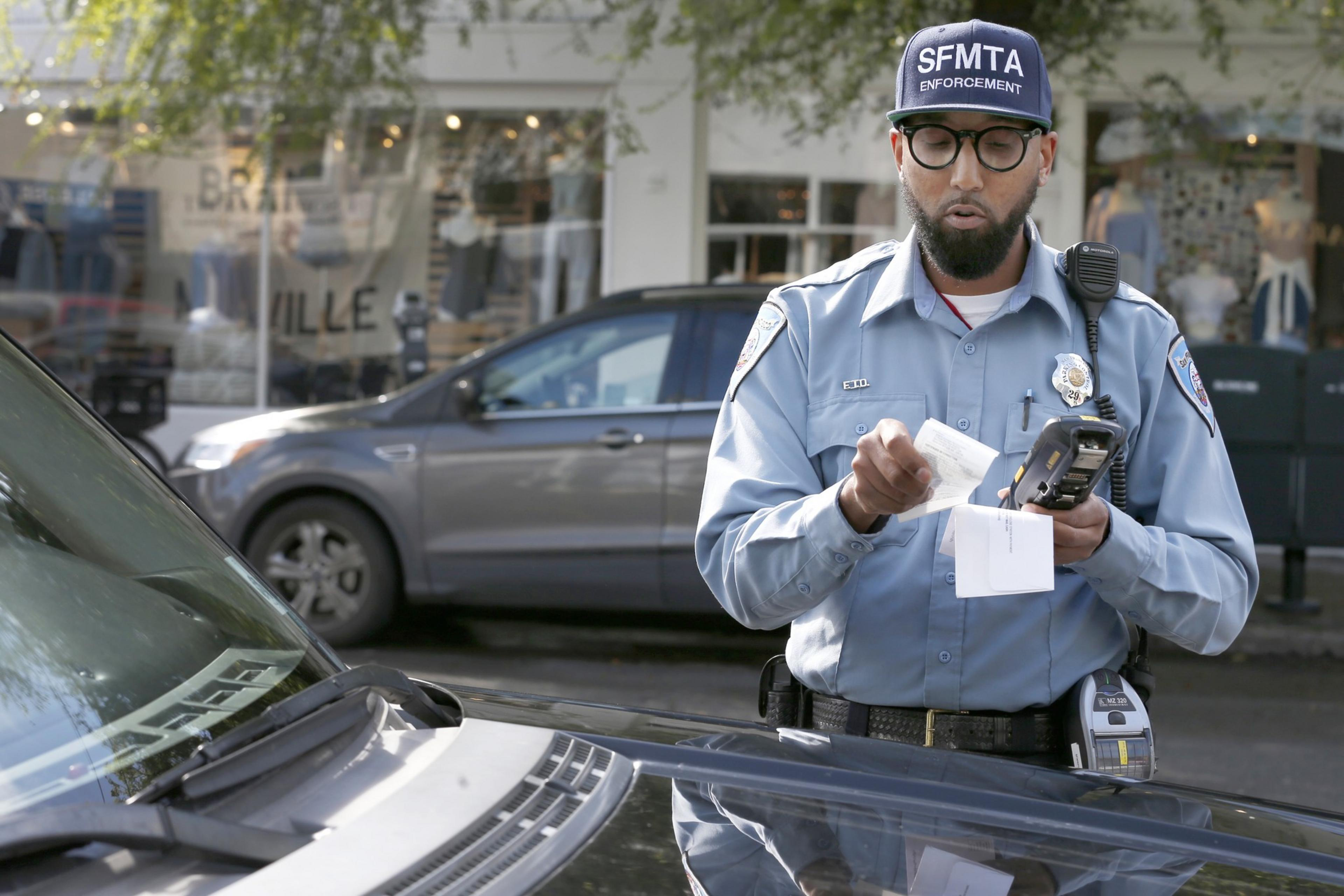 A man holding a device prints out a ticket in front of a vehicle.