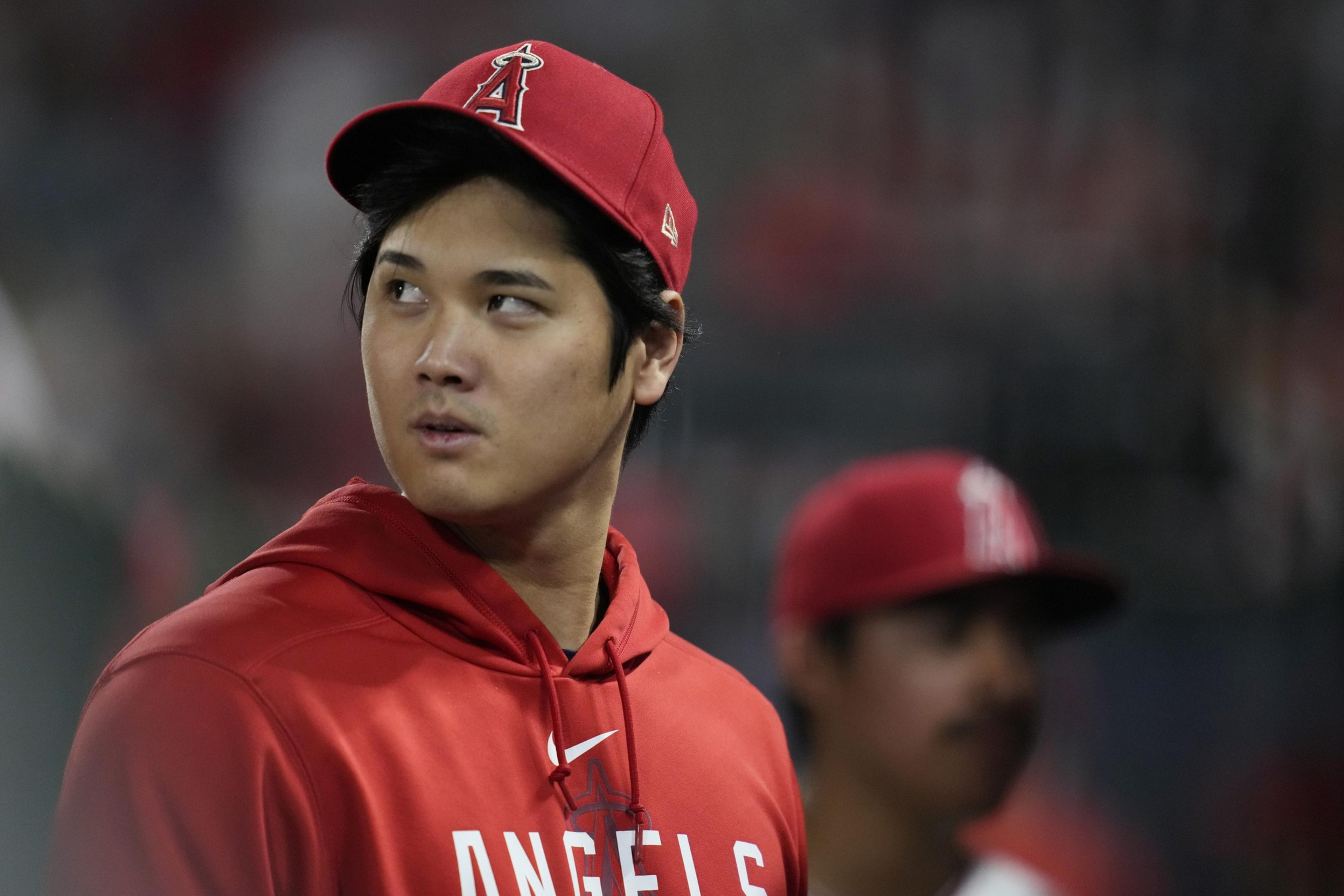 A baseball player in a red cap and red sweatshirt looks past his right shoulder