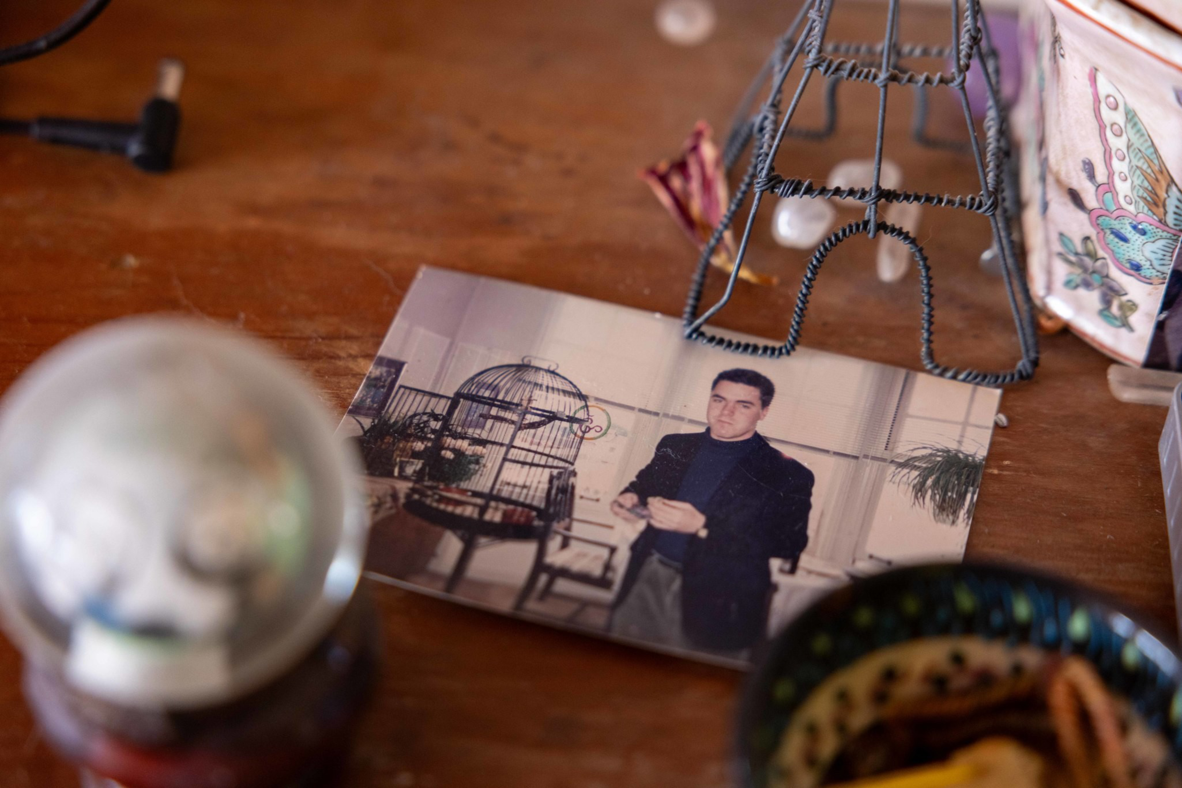 A photo of a man in a dark jacket stands on a wooden surface surrounded by a small Eiffel Tower model, a birdcage, and various decorative items.