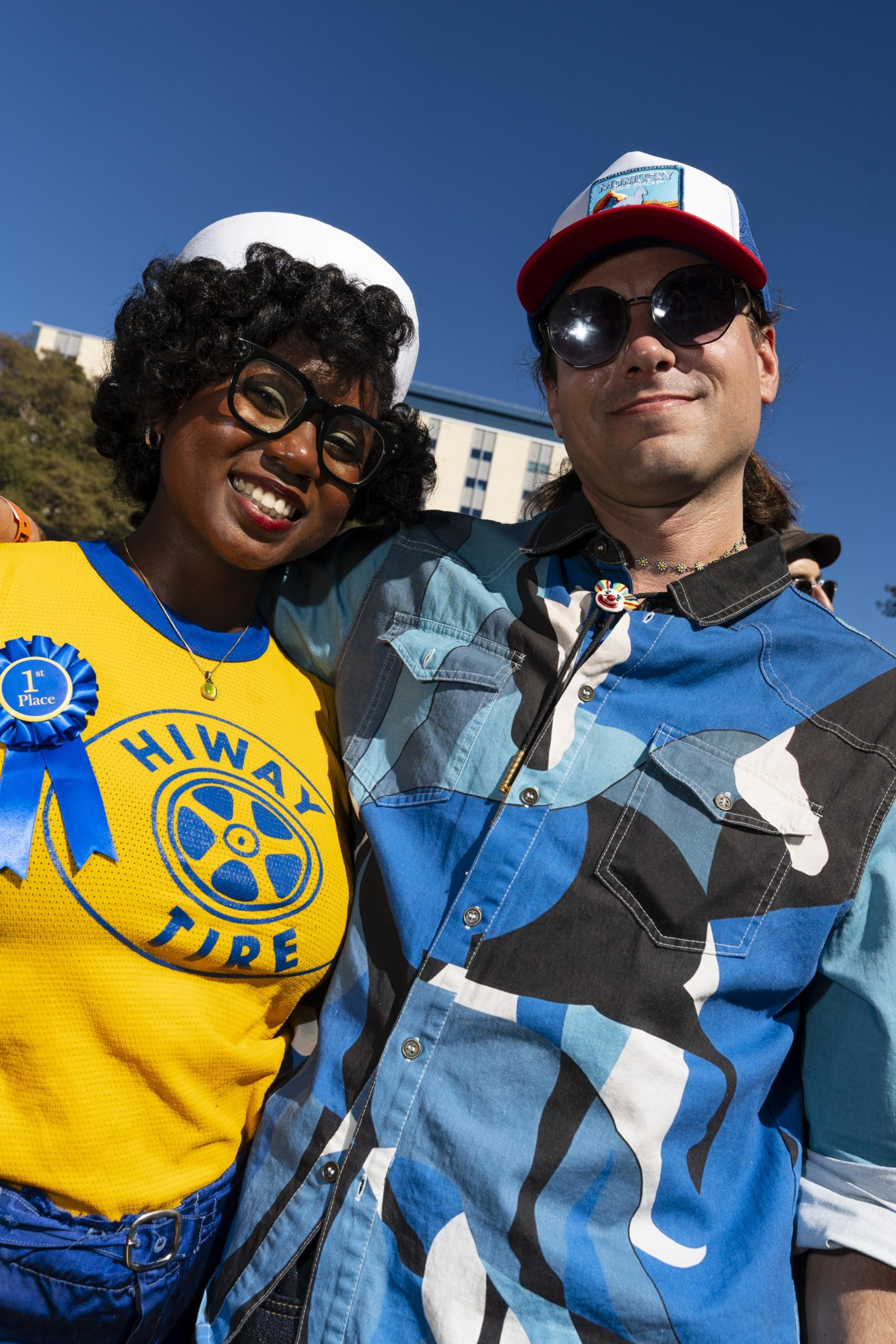 Two people stand closely, smiling under a clear blue sky. One wears a yellow &quot;Hiway Tire&quot; shirt with a 1st place ribbon; the other sports a blue patterned shirt.