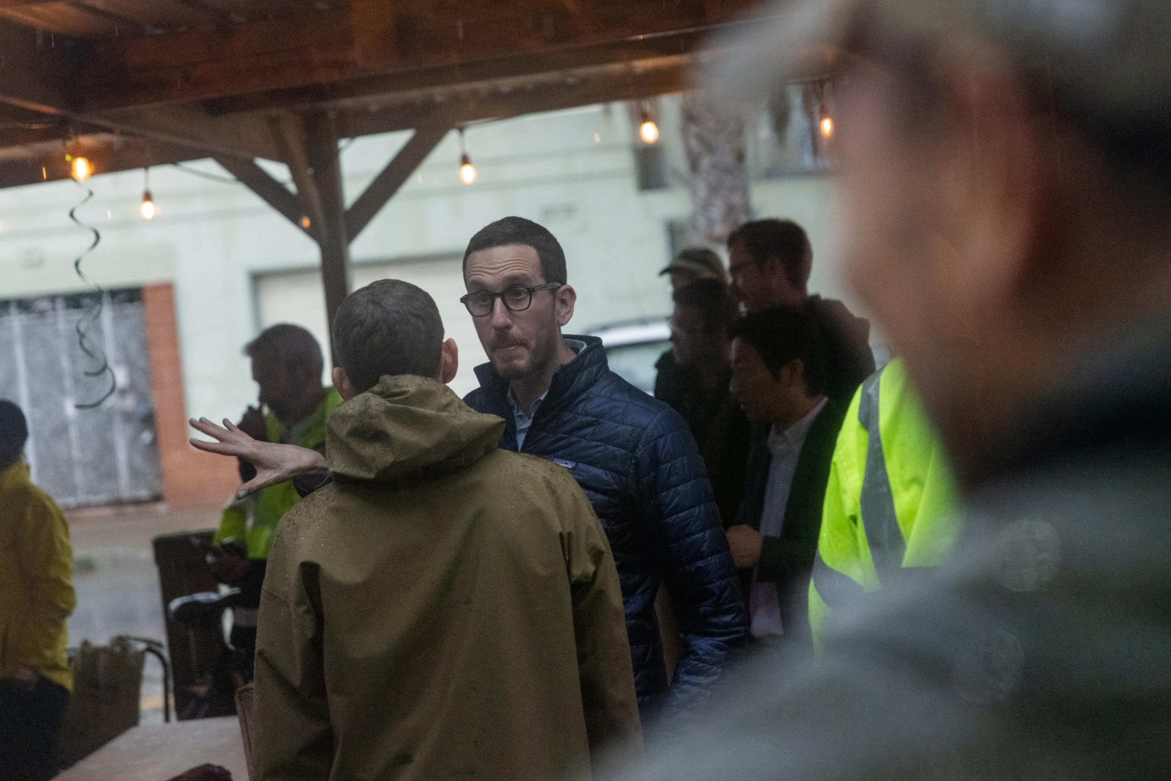 Senator Scott Wiener talking with a person under shelter in the rain.