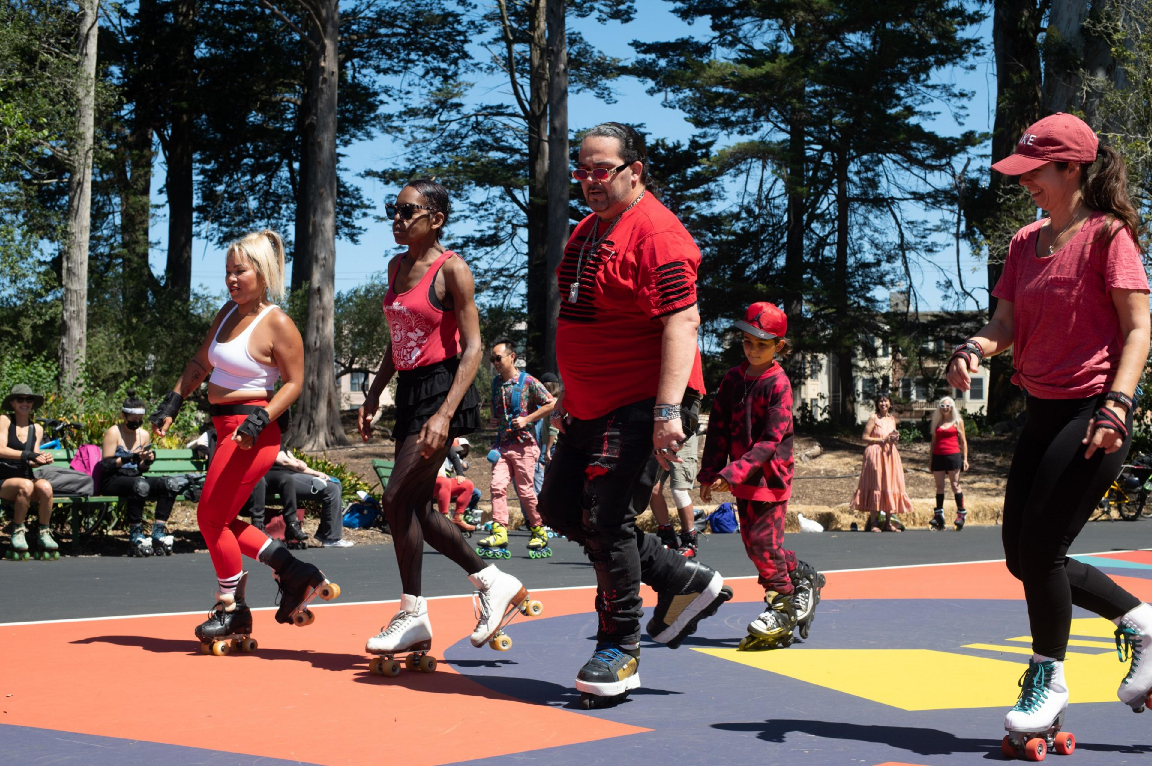 People in colorful attire are roller skating on a vibrant outdoor rink under a clear sky.