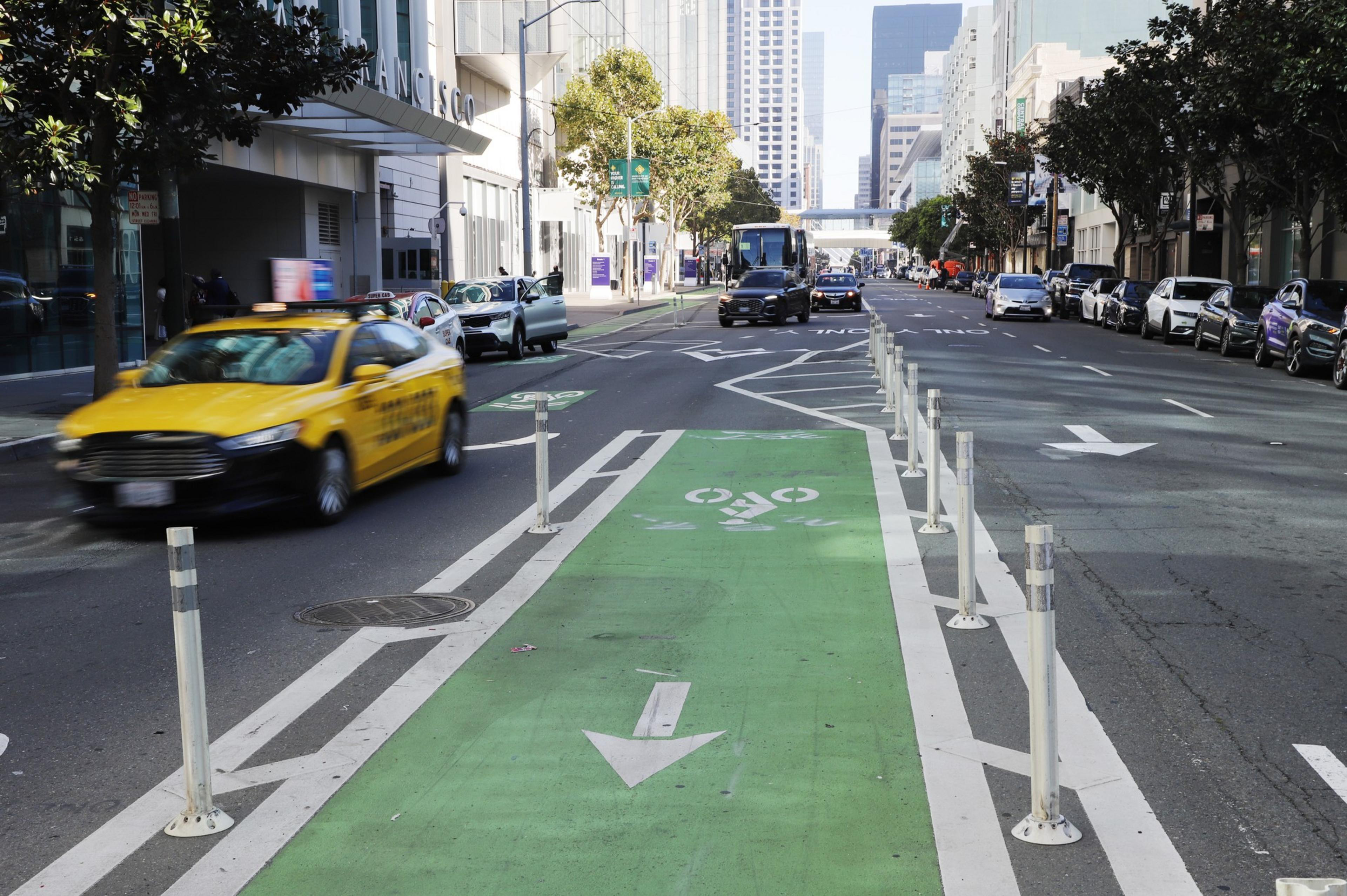 A taxi and a few other vehicle drive down Howard Street in San Francisco with a bike lane separating the lanes