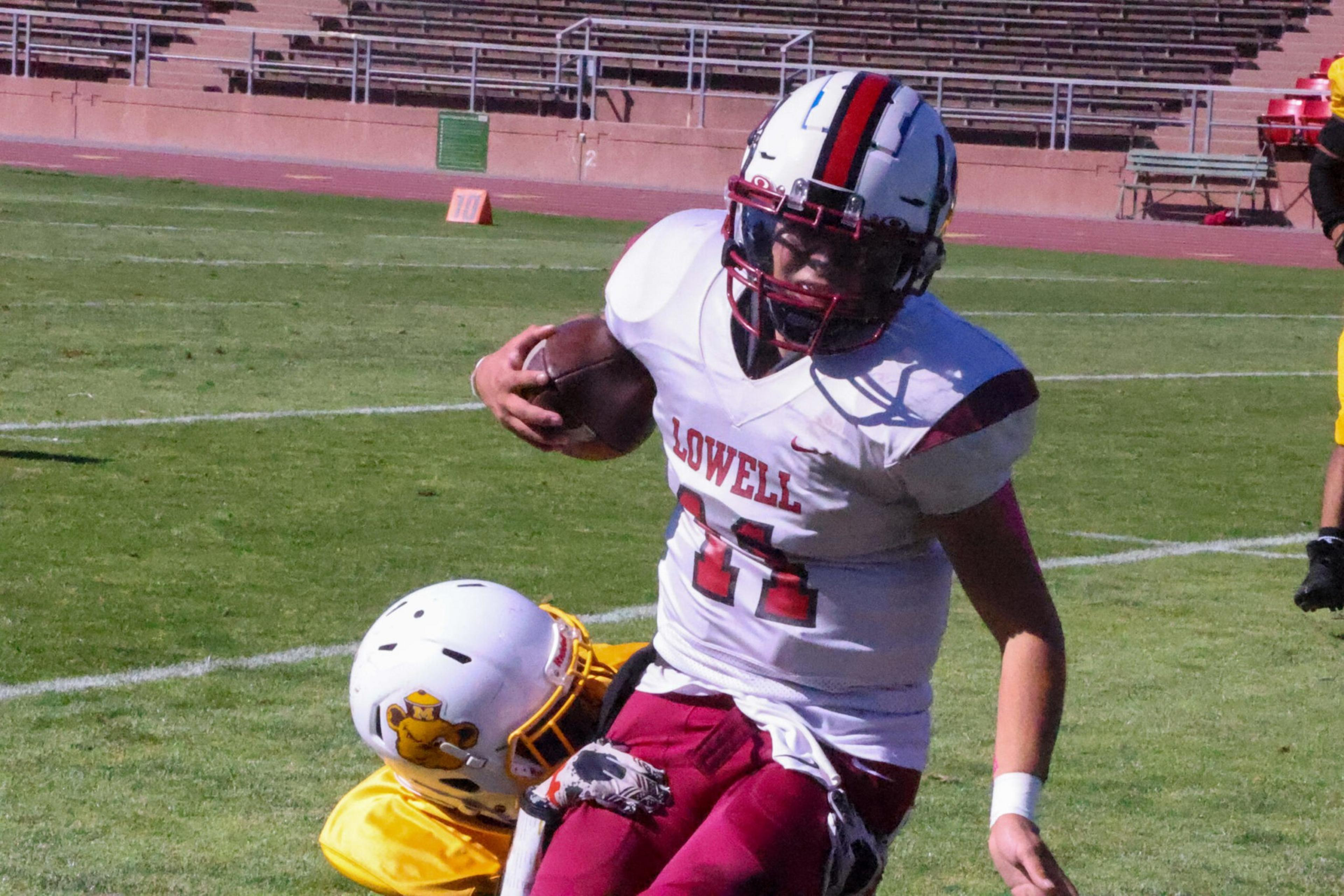 A football player wearing a white jersey with "Lowell" and number 11 runs with the ball while being tackled by a player in a yellow uniform.