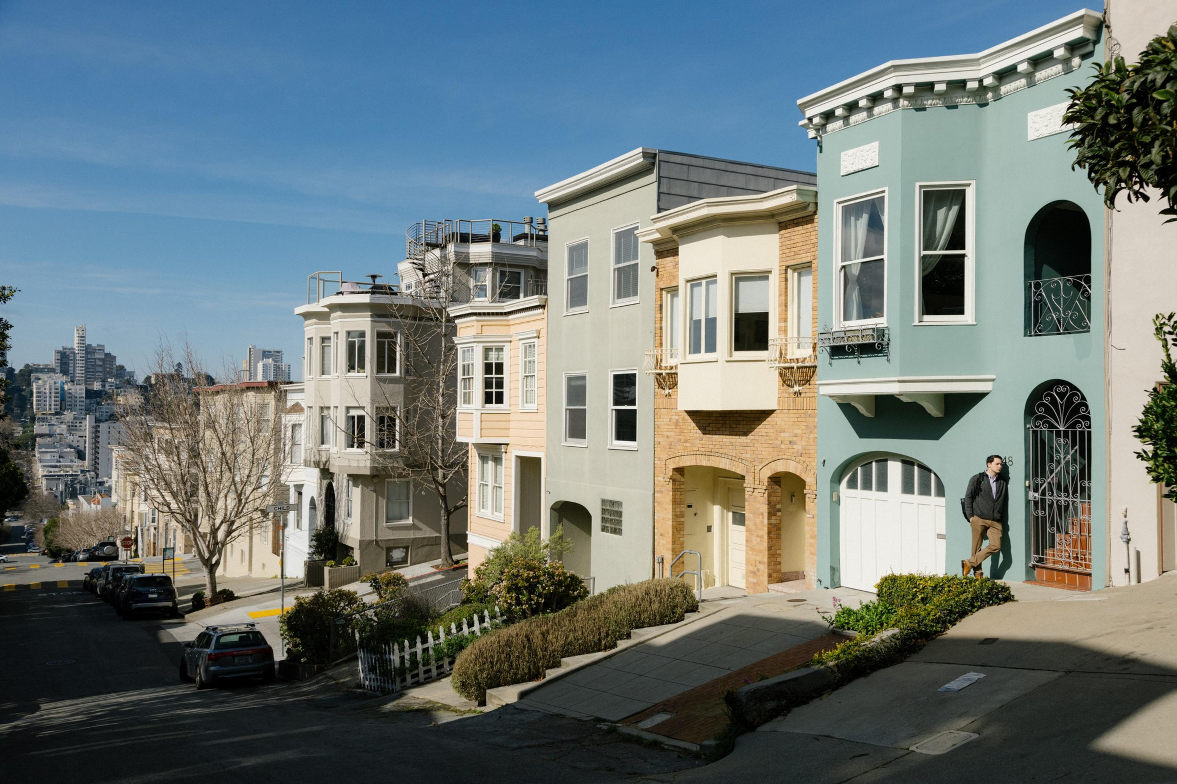 Row of colorful townhouses on a steep street with a person walking and clear skies.