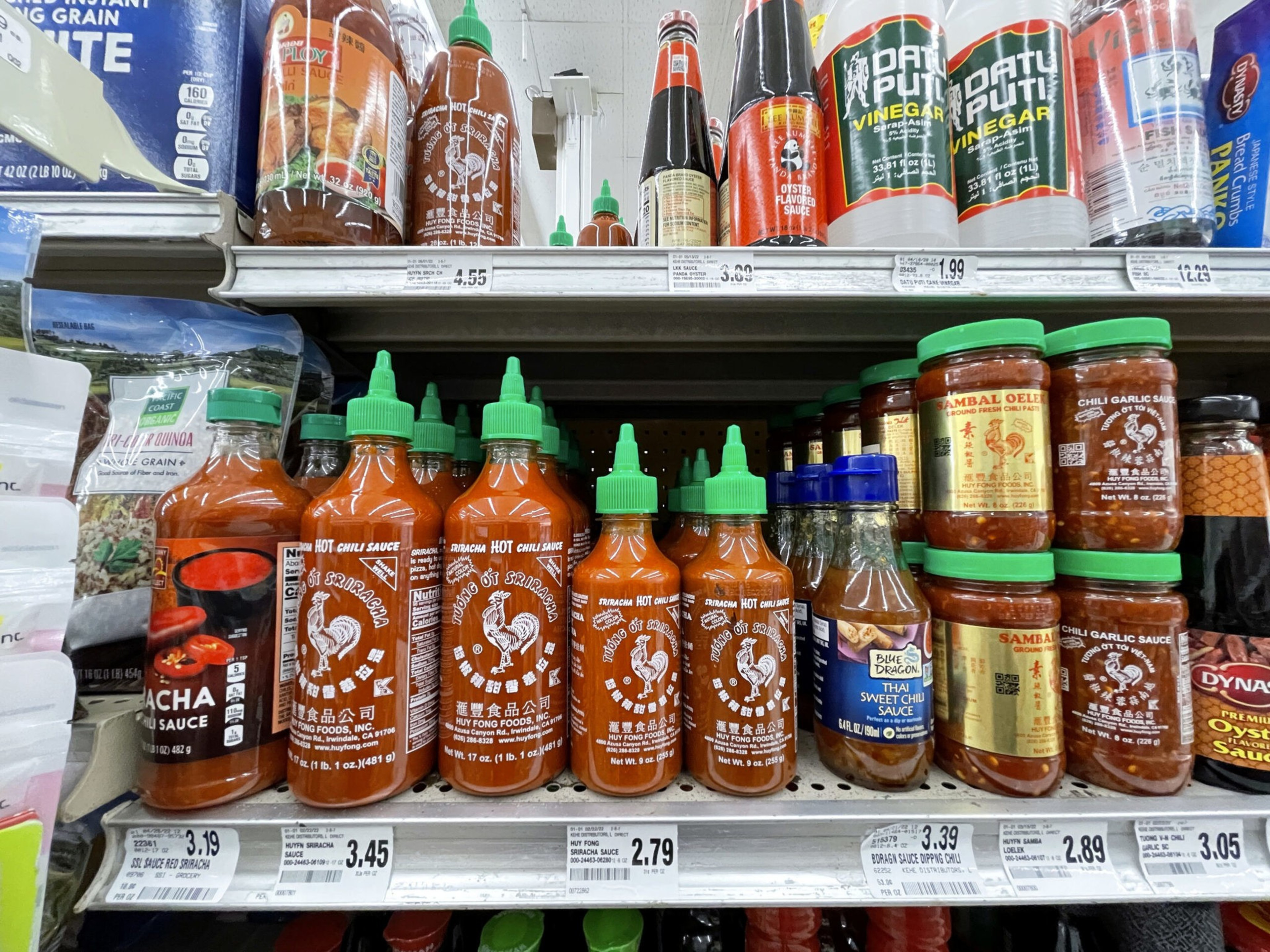 Bottles of Sriracha hot chili sauce, sambal oelek, chili garlic sauce, sweet chili sauce, vinegar, and oyster sauce on store shelves.