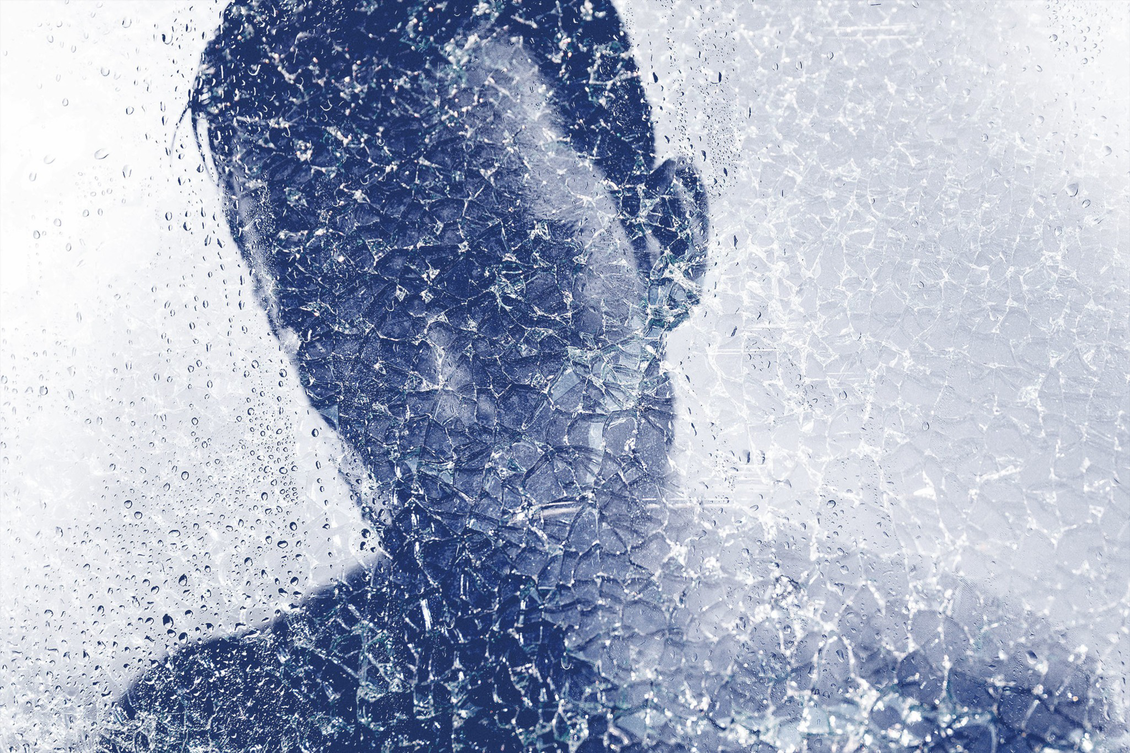 A person's silhouette appears blurred behind cracked glass with water droplets, creating a fragmented and abstract effect.