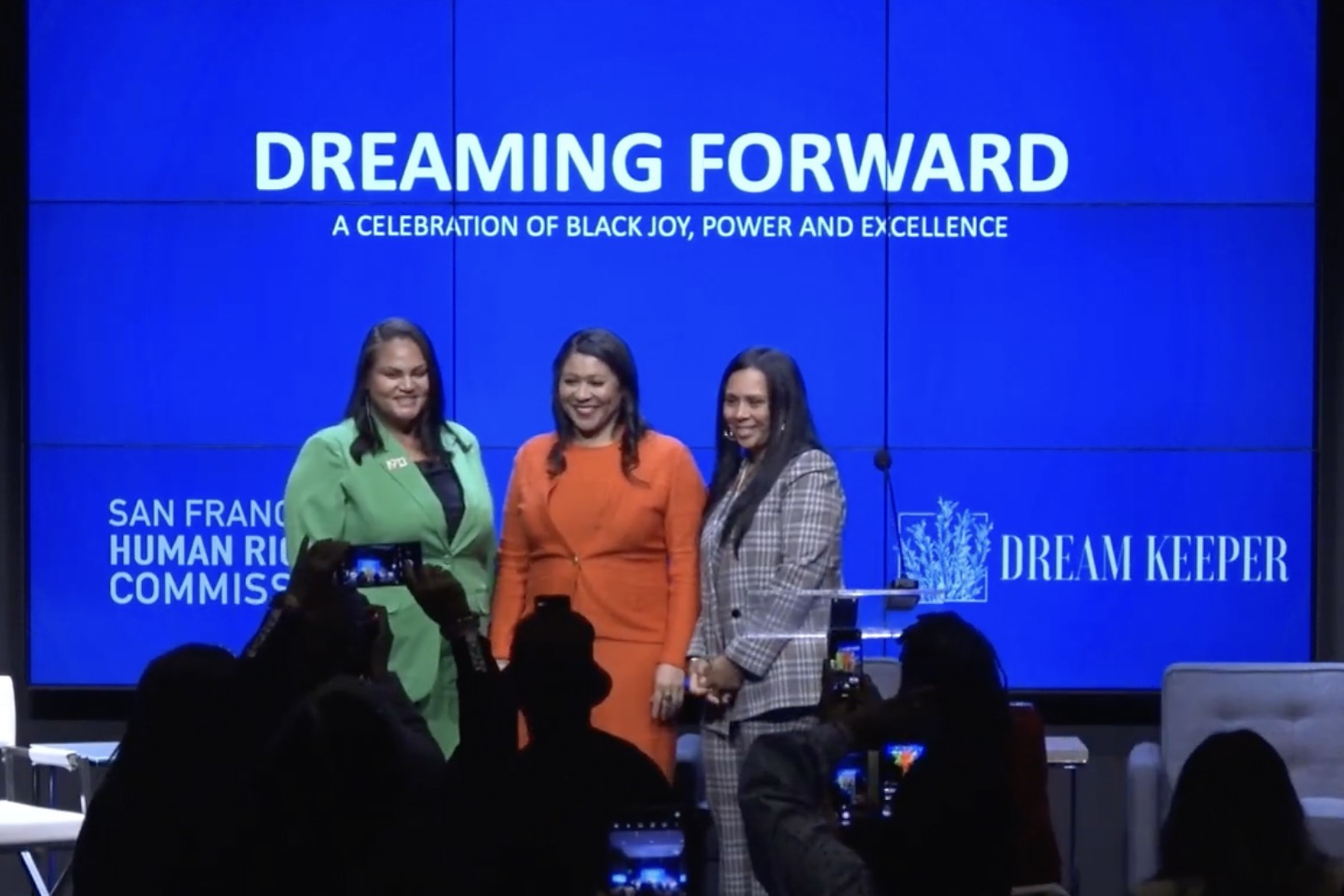 Three people stand on a stage with the words &quot;Dreaming Forward&quot; in the background.