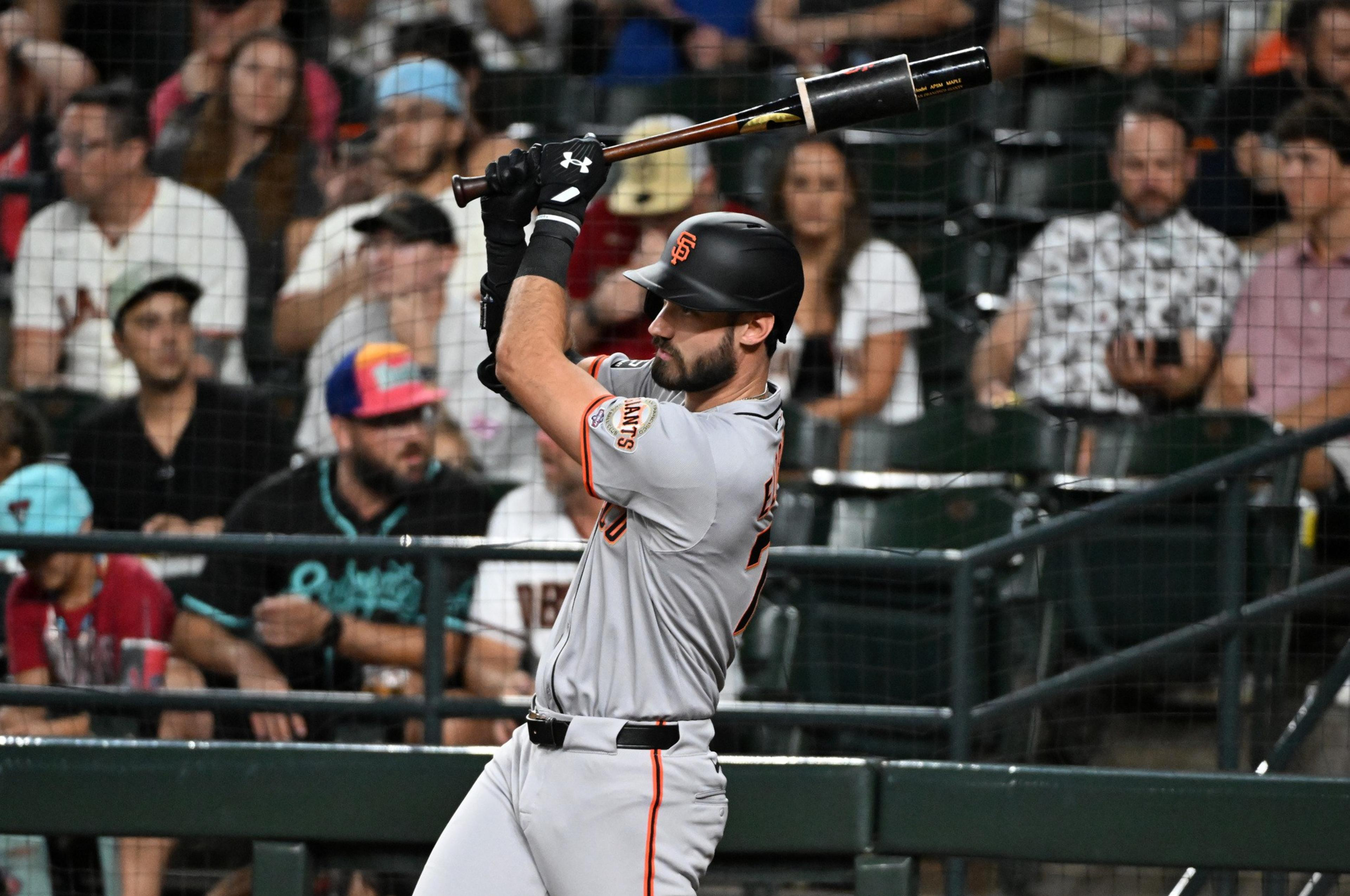 A baseball player in a gray San Francisco Giants uniform prepares to swing a bat as spectators watch from behind a protective net.