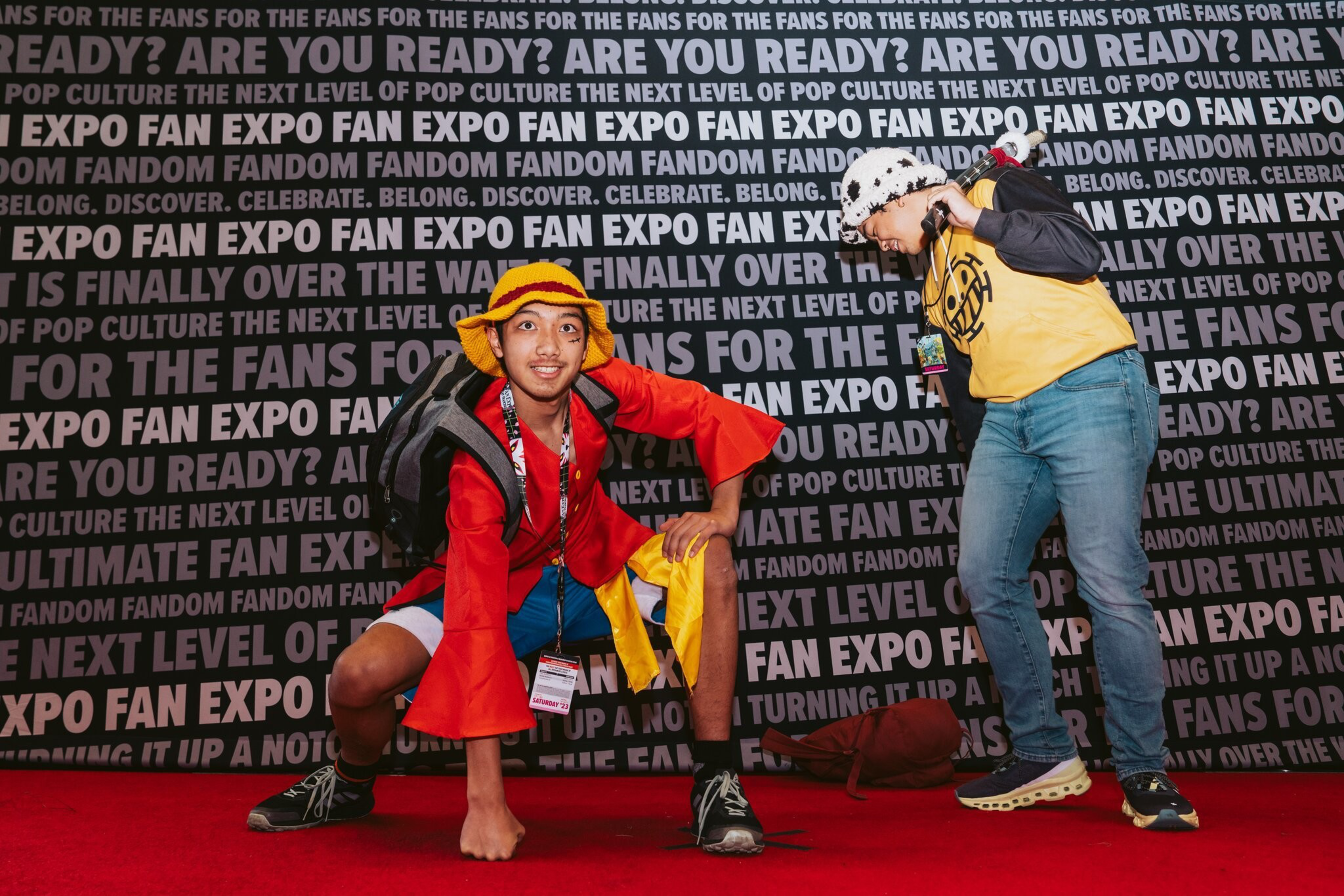 Two costumed men crouch in front of a step and repeat on a red carpet.