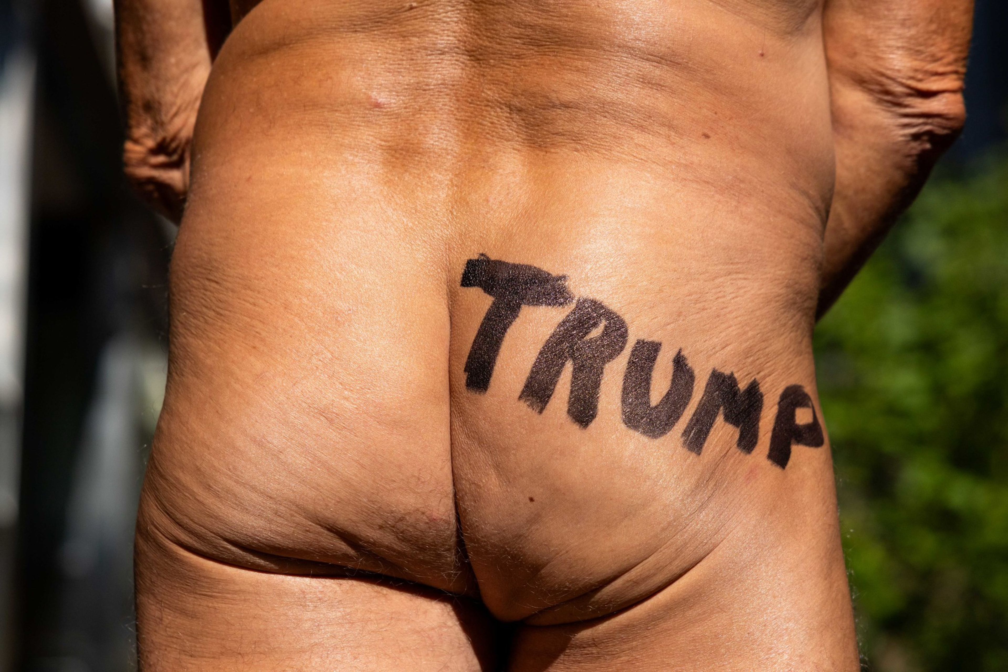 The word “TRUMP” is painted in black letters across the bare buttocks of a person standing outdoors.