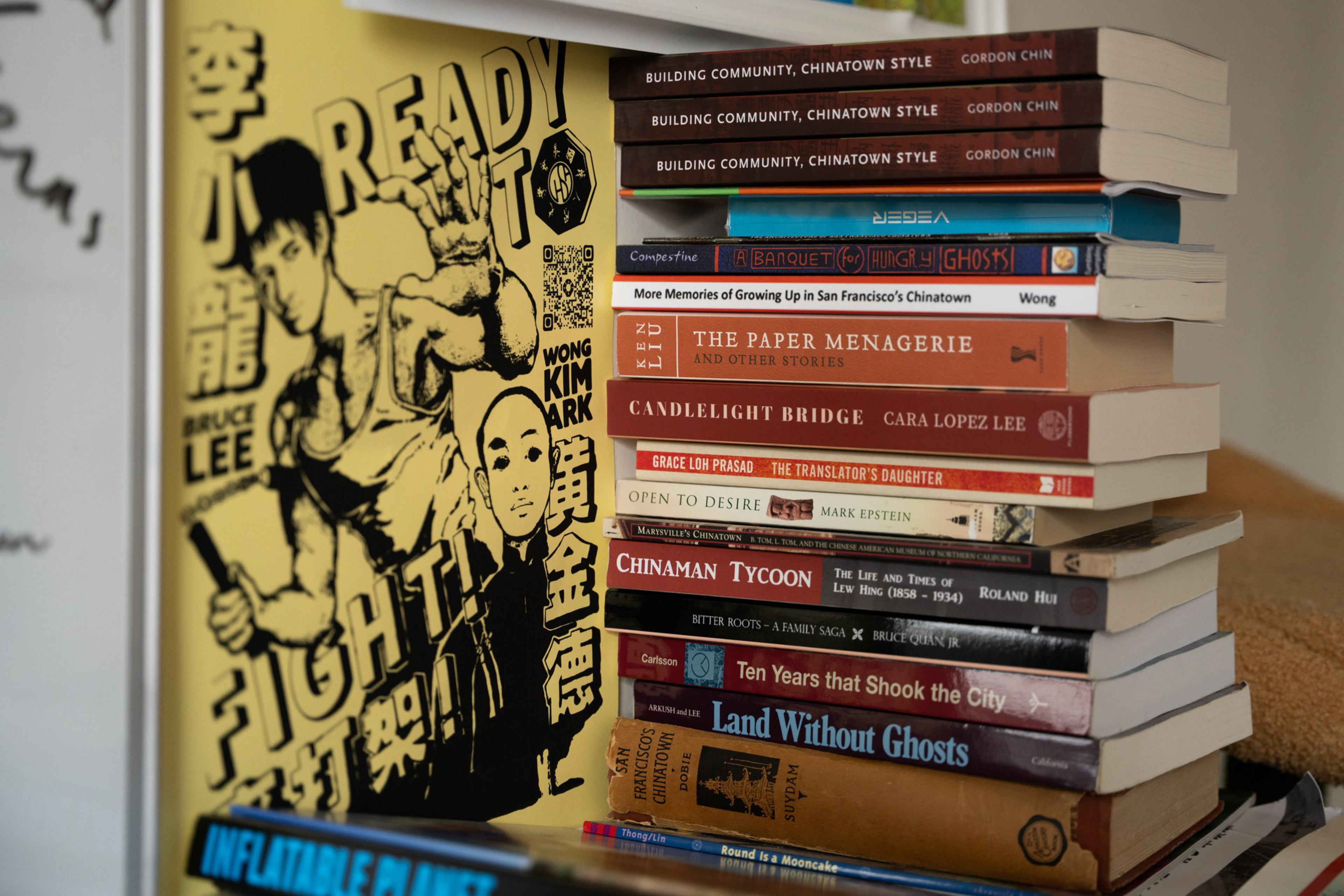 A stack of books with titles on Asian American culture and history, alongside a poster-like image of Bruce Lee and Wong Kim Ark with the words “Ready to Fight!”