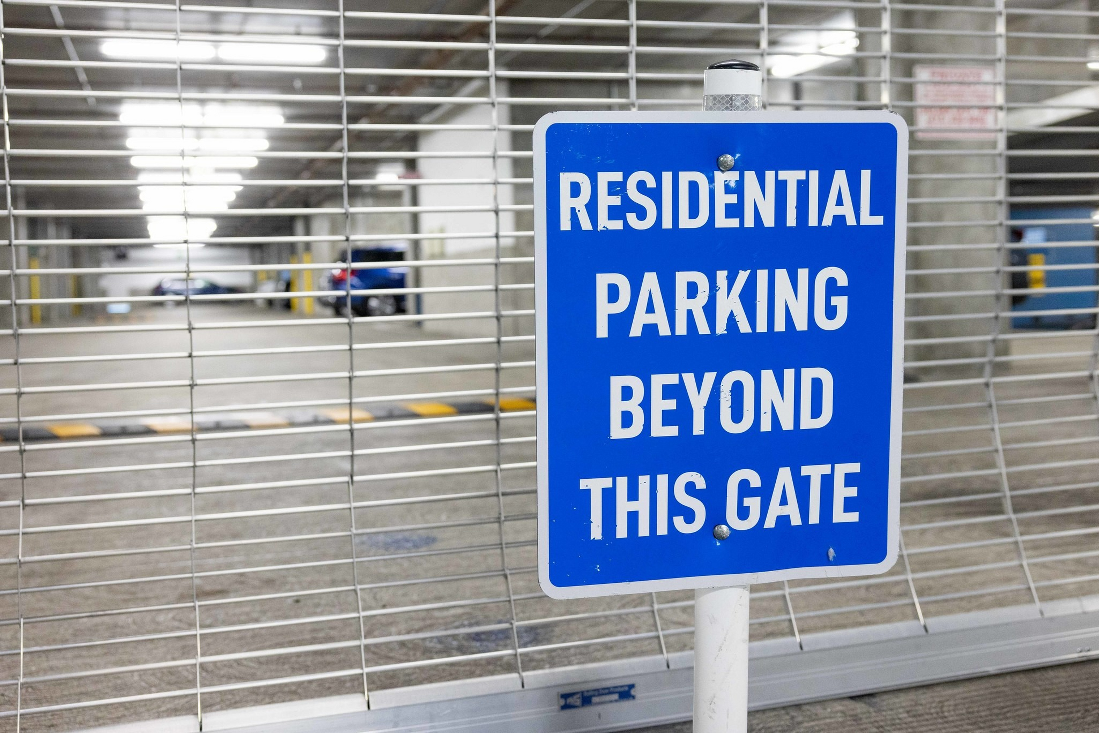 A blue sign with white text reads “Residential parking beyond this gate” in front of a closed metal gate blocking a parking garage.