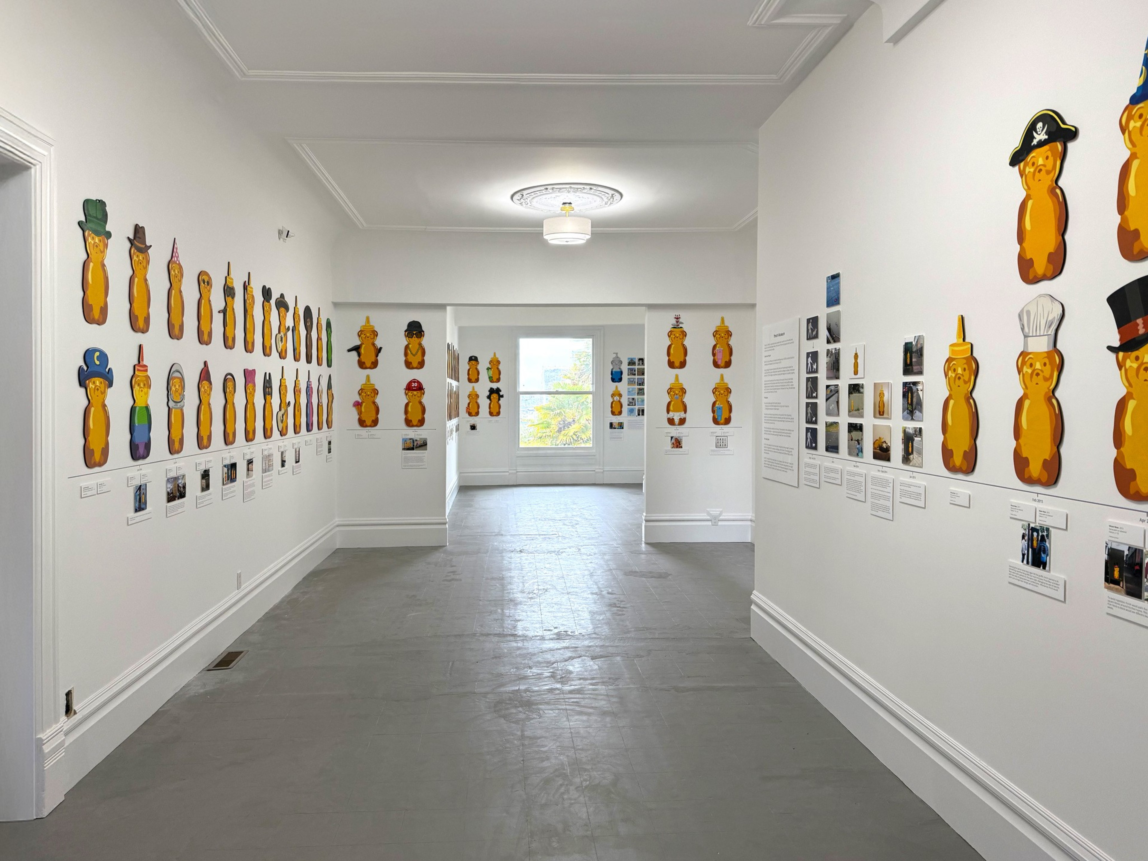 The image shows a gallery with walls displaying numerous cartoonish honey bears in various costumes, each accompanied by photos and descriptions beneath them.