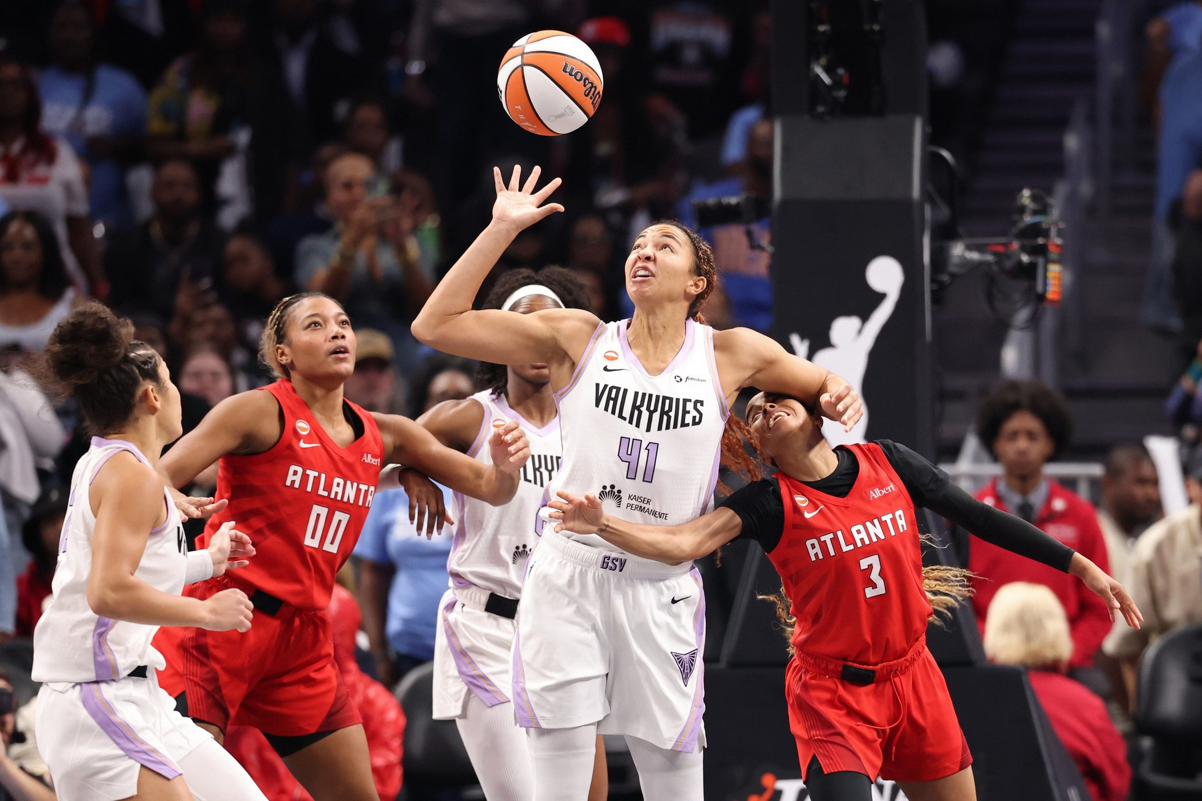 A basketball player in a white Valkyries jersey reaches up as two players in red Atlanta jerseys try to block her during a game.