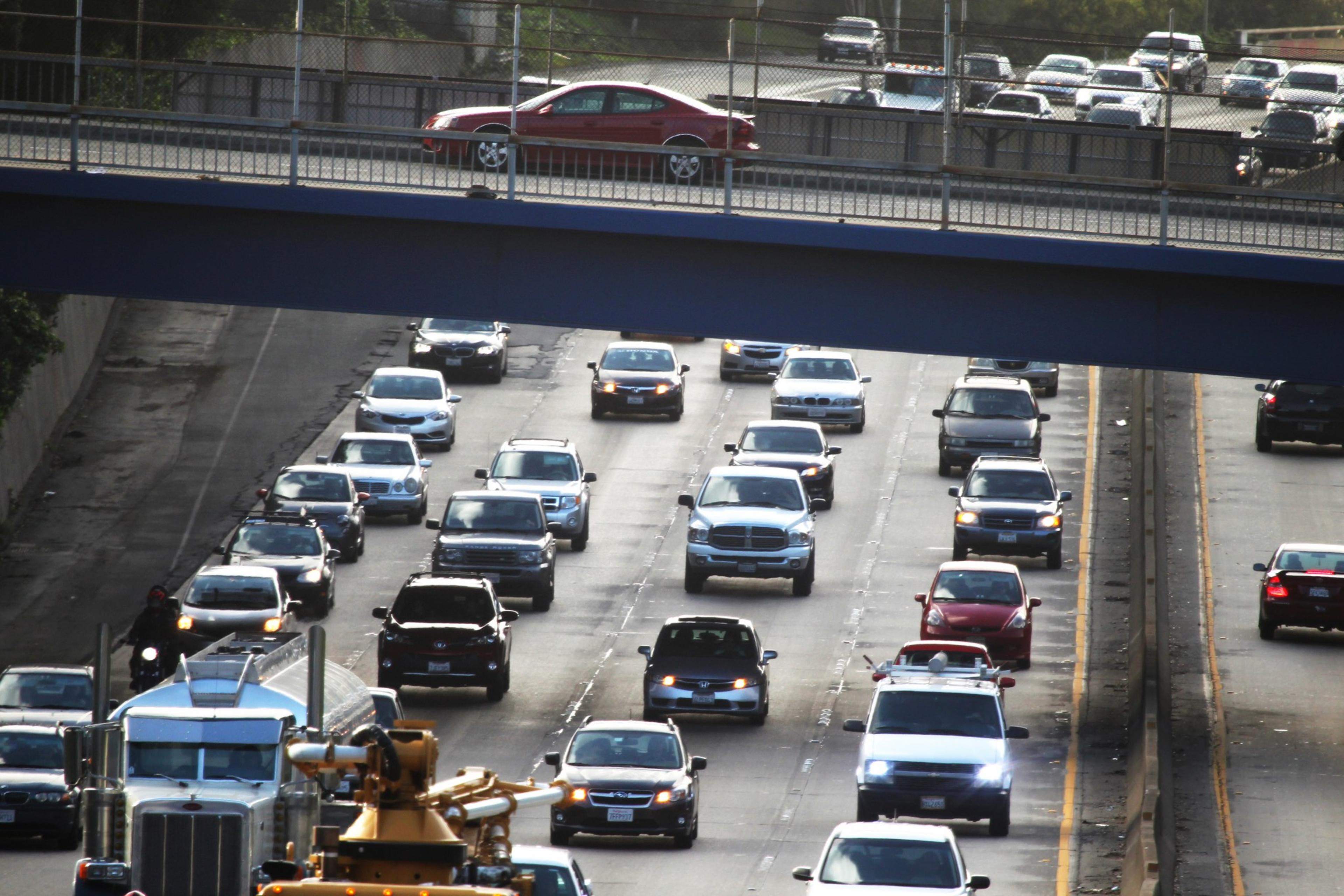 The image shows heavy traffic on a multi-lane highway with various cars and a truck moving in both directions. An additional road runs overhead.
