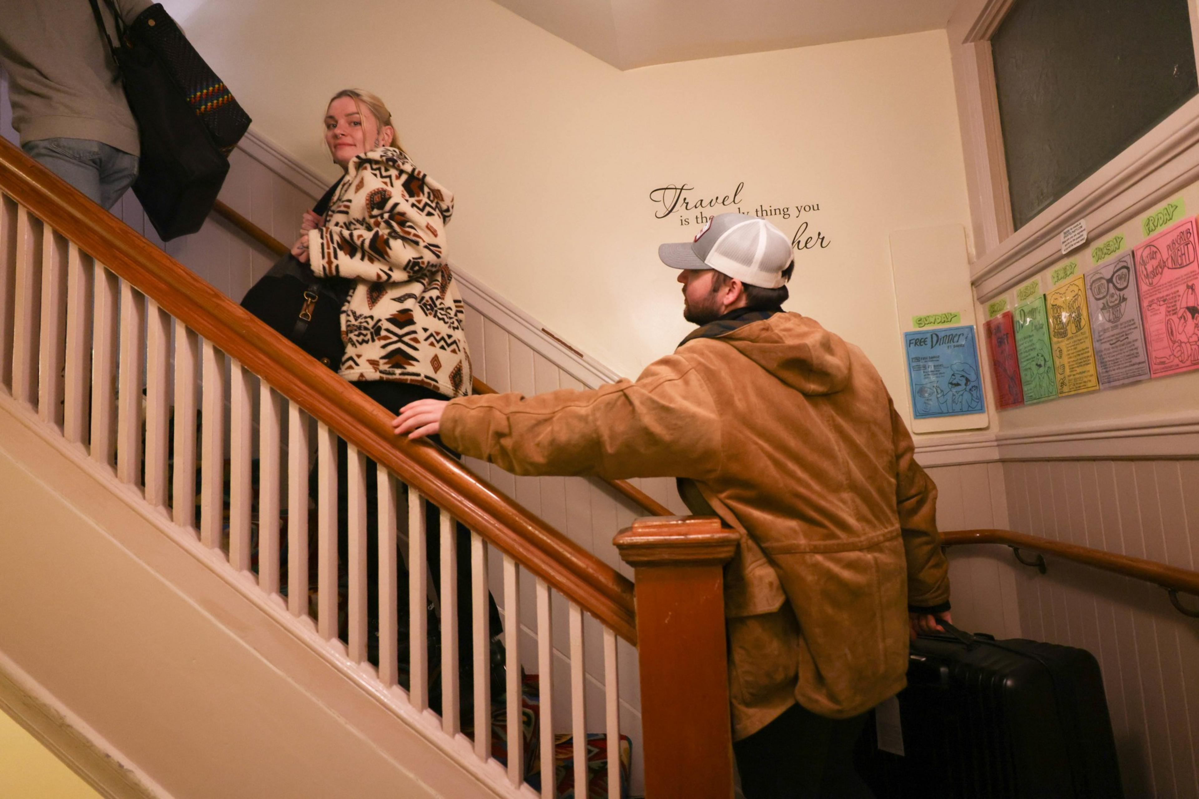Two people on a stairway with suitcases, colorful posters on the wall, and a quote about travel.