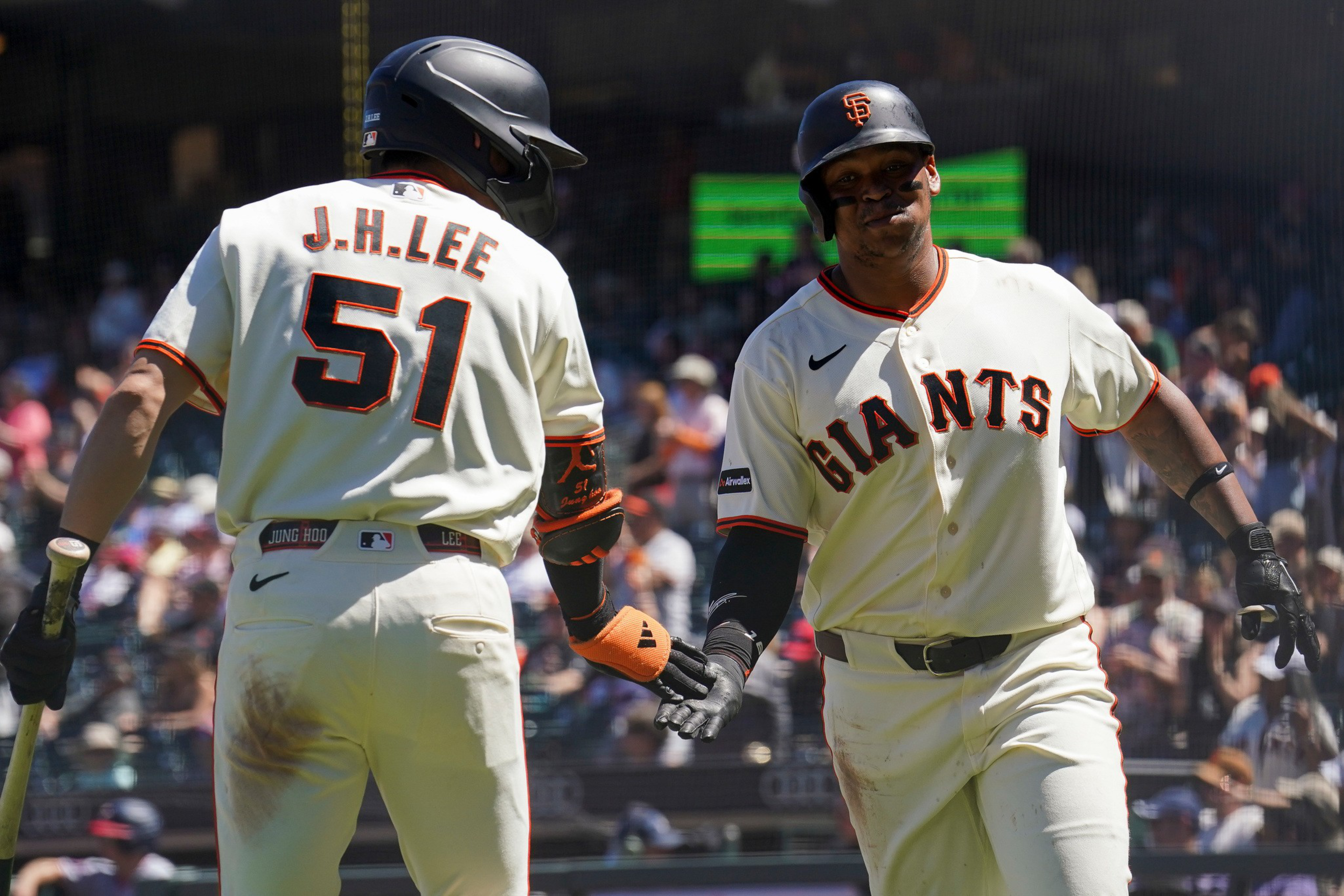 Two San Francisco Giants players in white uniforms with black and orange accents exchange a handshake during a baseball game.