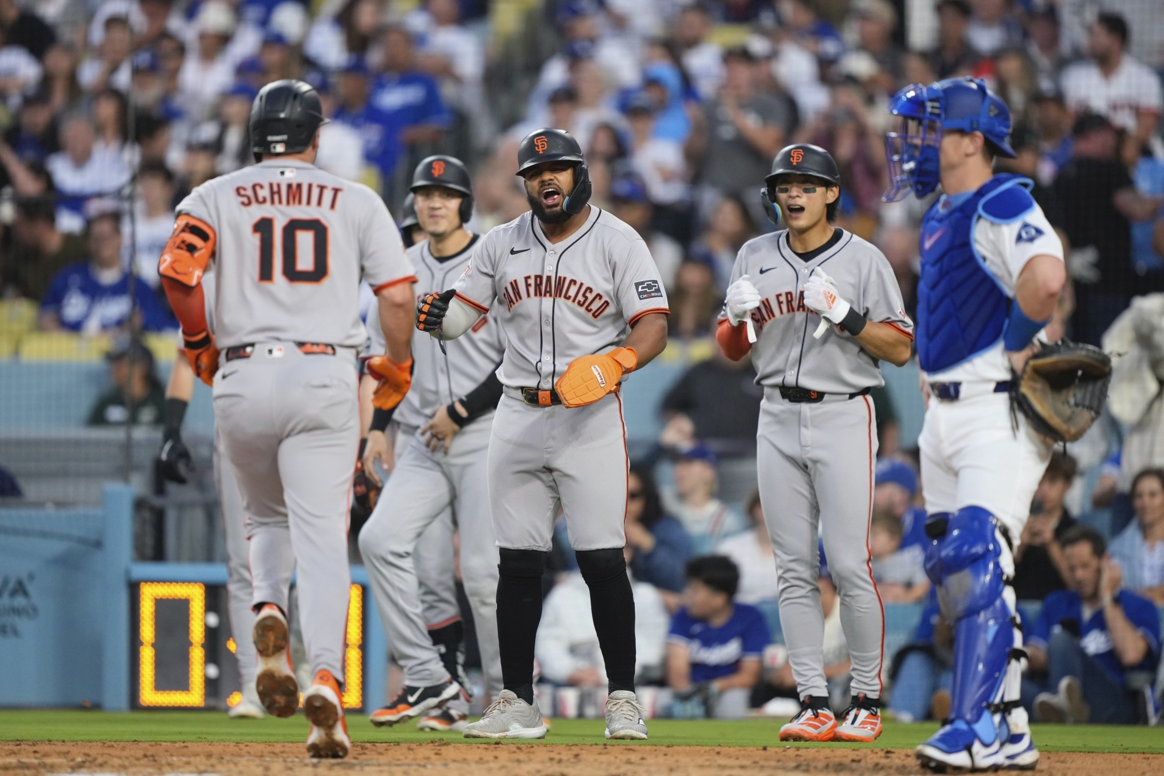 Baseball players in gray jerseys with "San Francisco" celebrate on the field, while a player in blue catcher gear stands nearby. The crowd watches in the background.