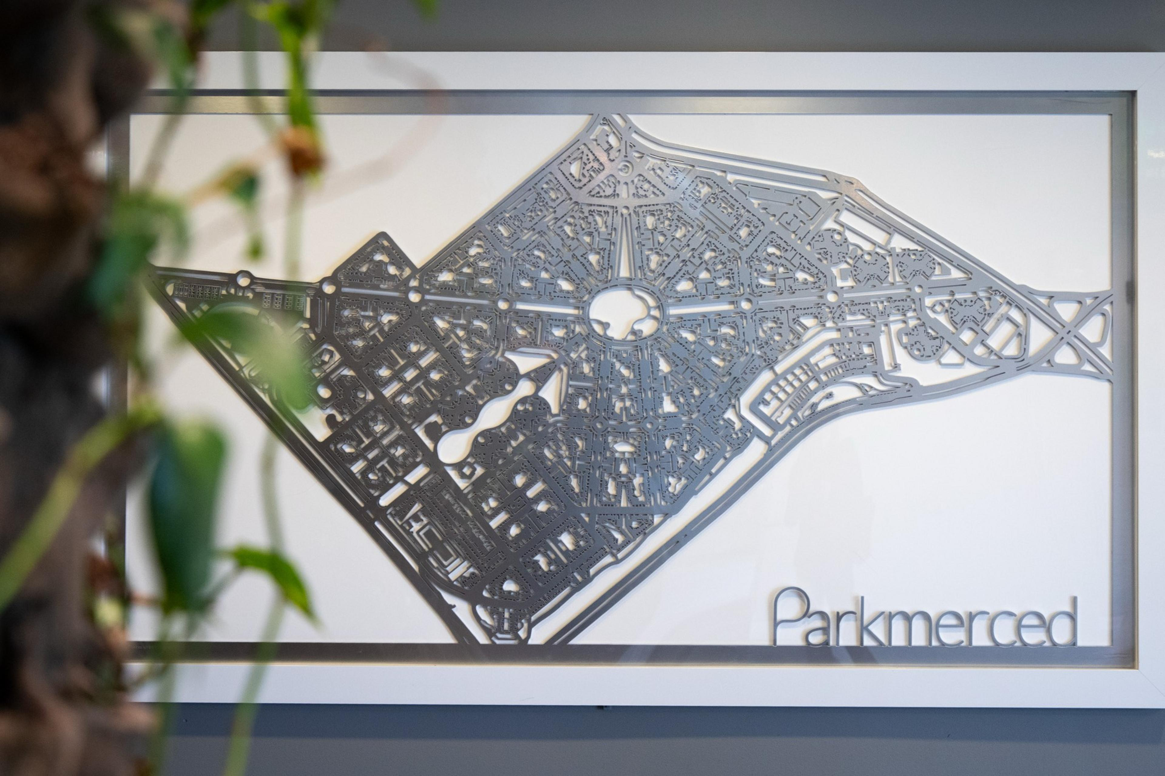 The image shows a framed, detailed map of Parkmerced, featuring intricate lines and shapes representing roads and structures, with a tree-like plant partially obscuring the left side.