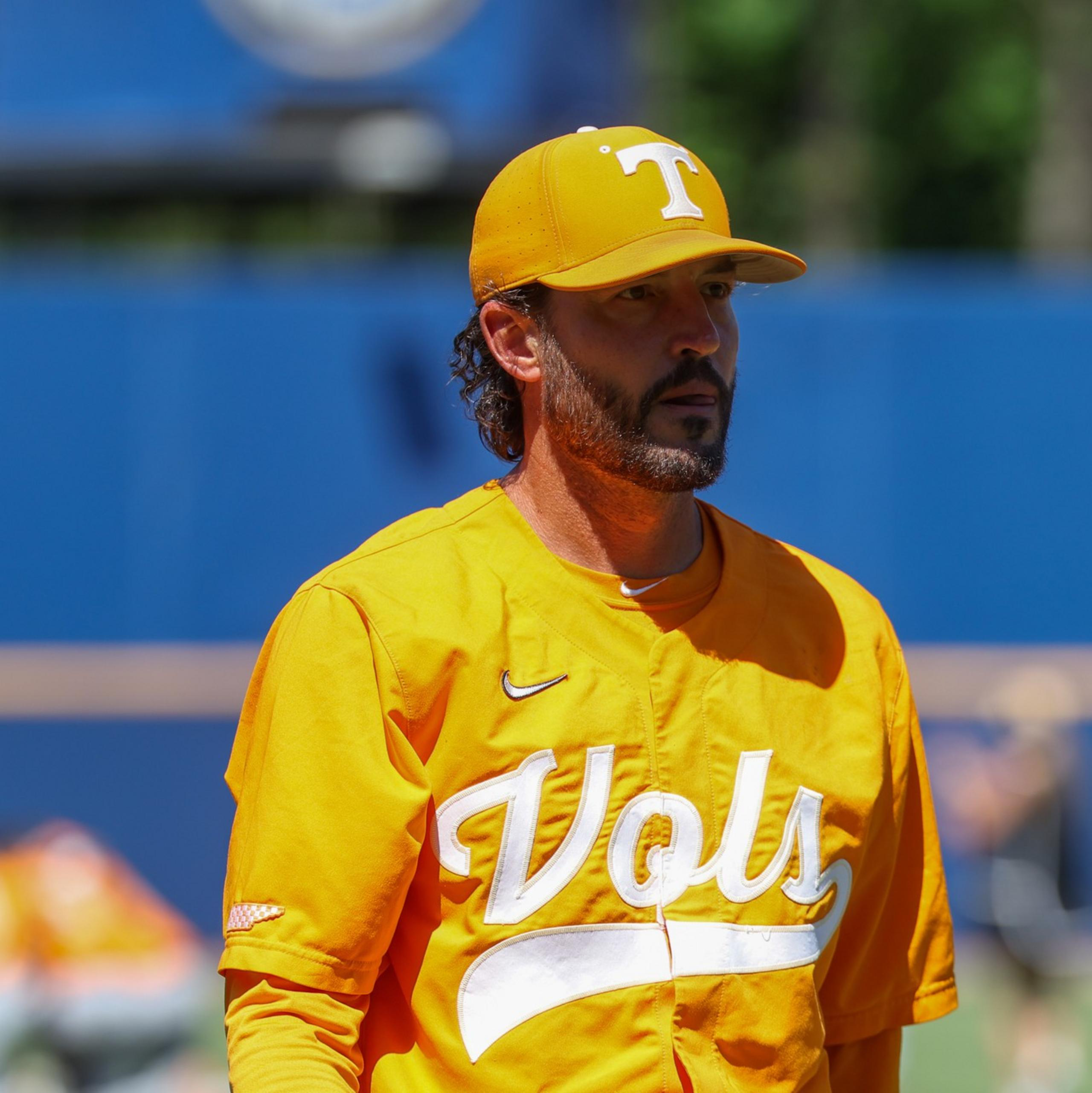 A man wearing a bright orange "Vols" baseball jersey and cap looks intently off to the side on a sunny day at a sports field.