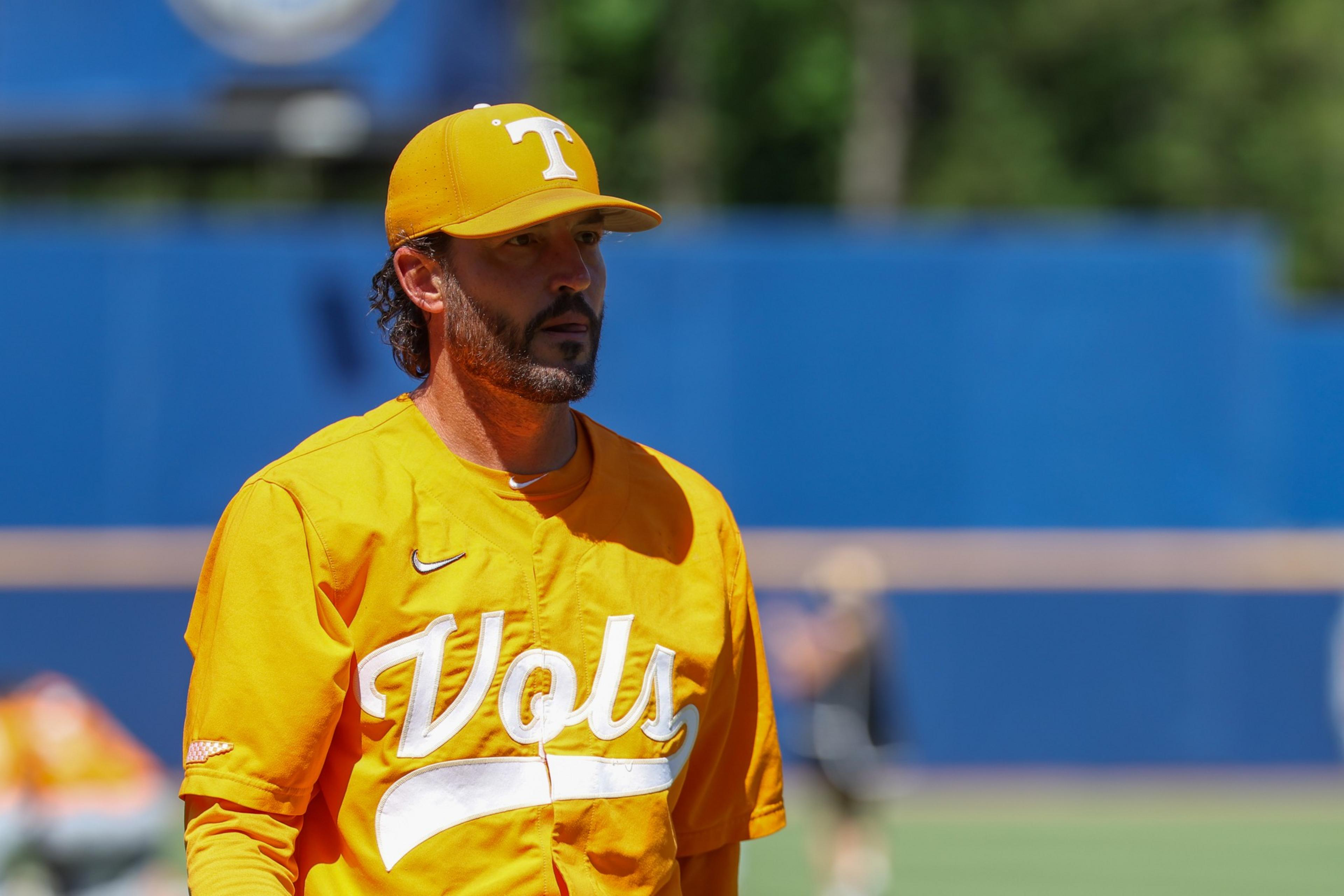 A man wearing a bright orange "Vols" baseball jersey and cap looks intently off to the side on a sunny day at a sports field.