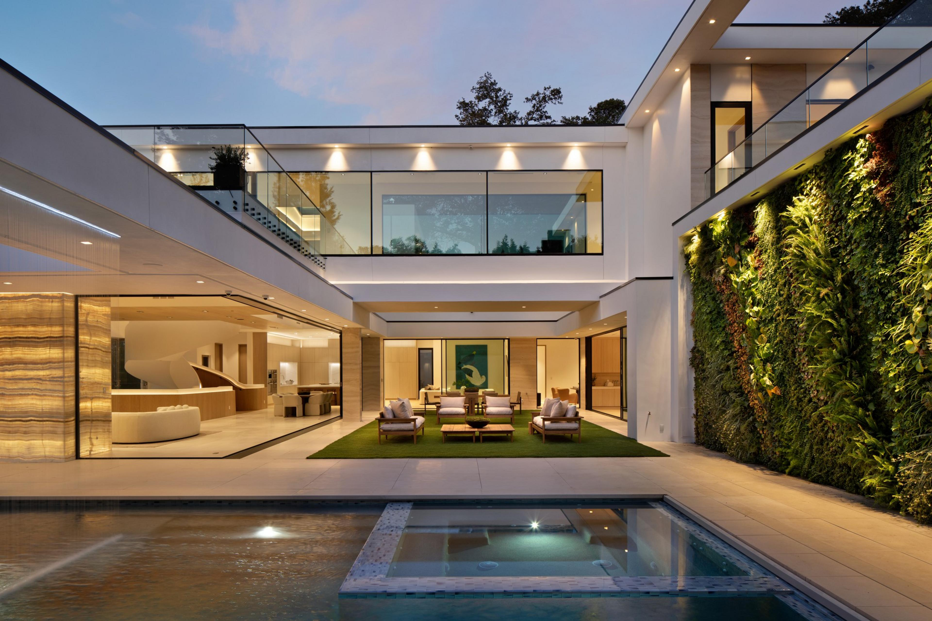 A modern house features an outdoor seating area on artificial grass, a wall covered with vertical greenery, and a pool with a built-in hot tub.