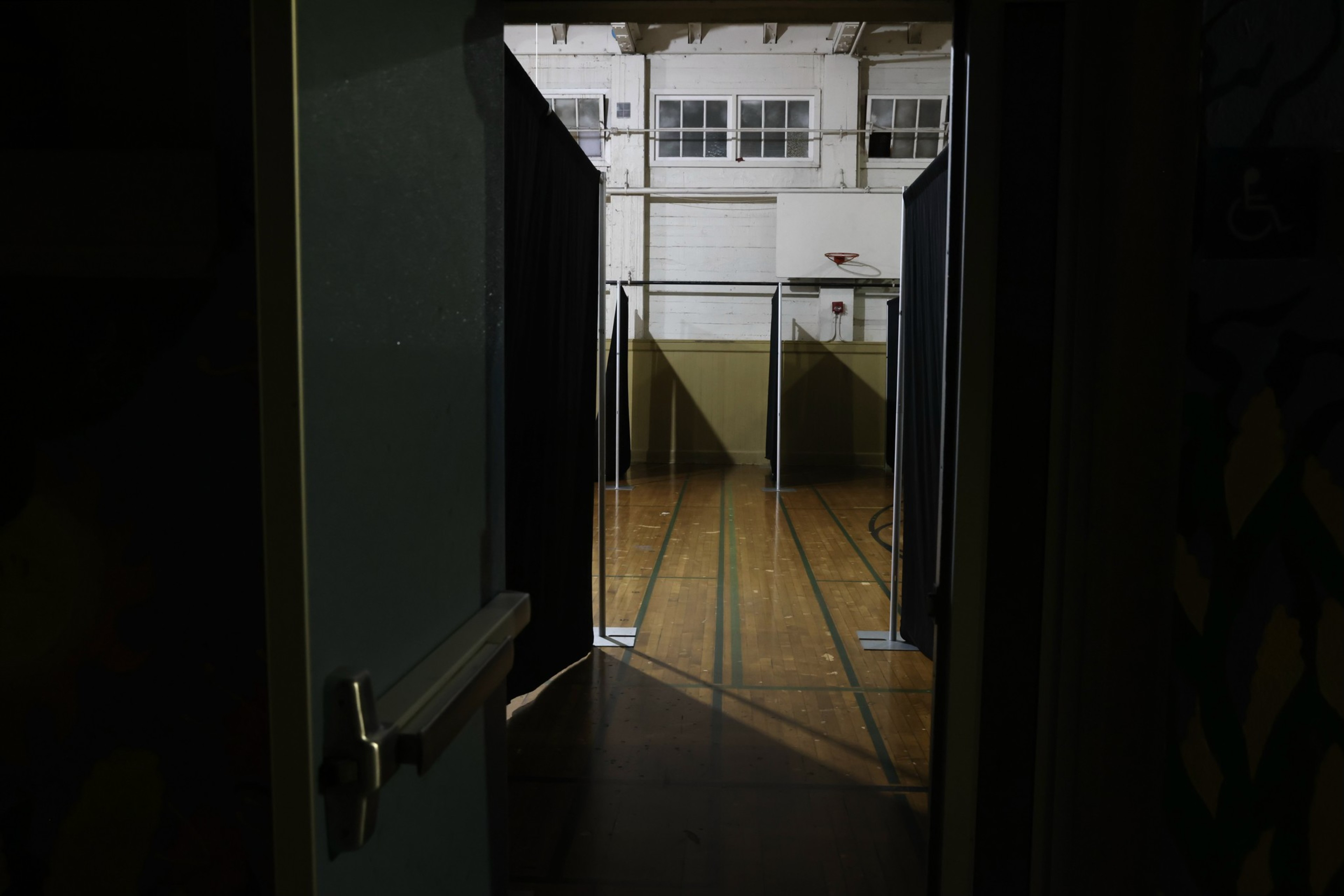 An old basketball gym with blue curtains lined up for people to sleep in.