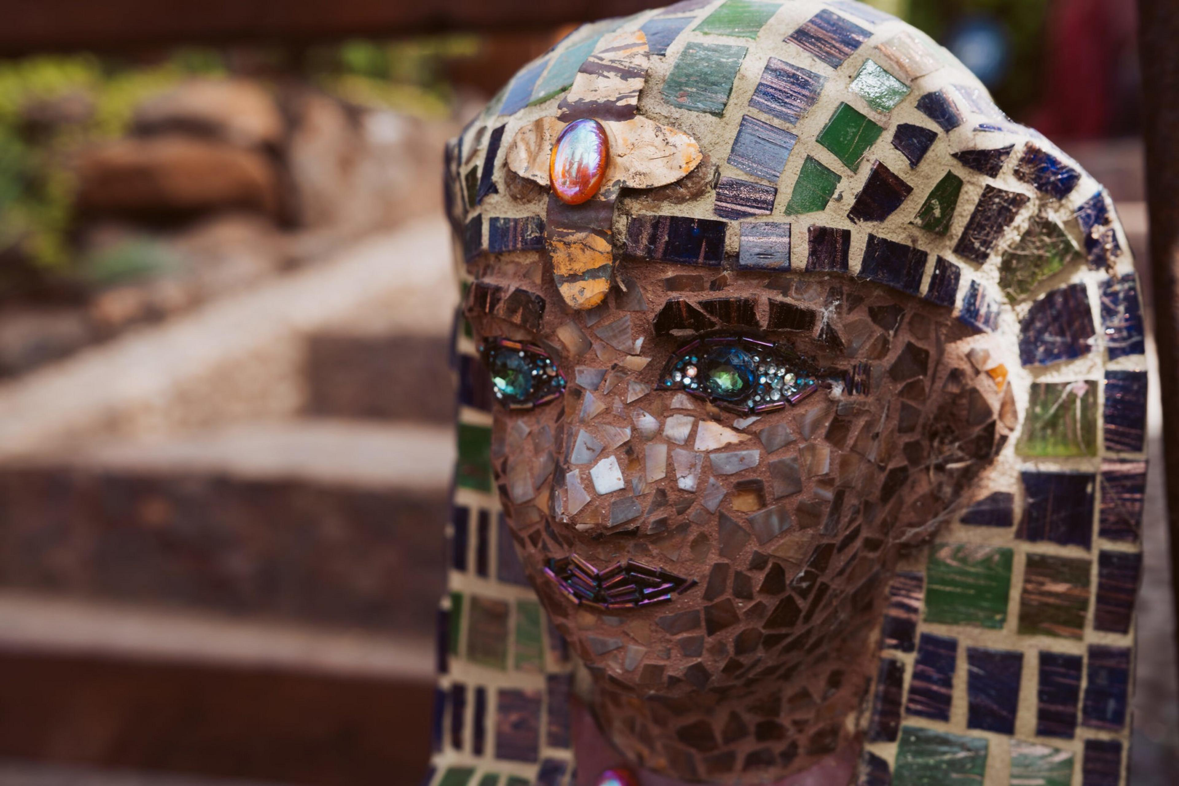 A detailed mosaic bust of an ancient Egyptian figure with green and blue tiles adorns the headdress and face, featuring a central amber-colored gem.