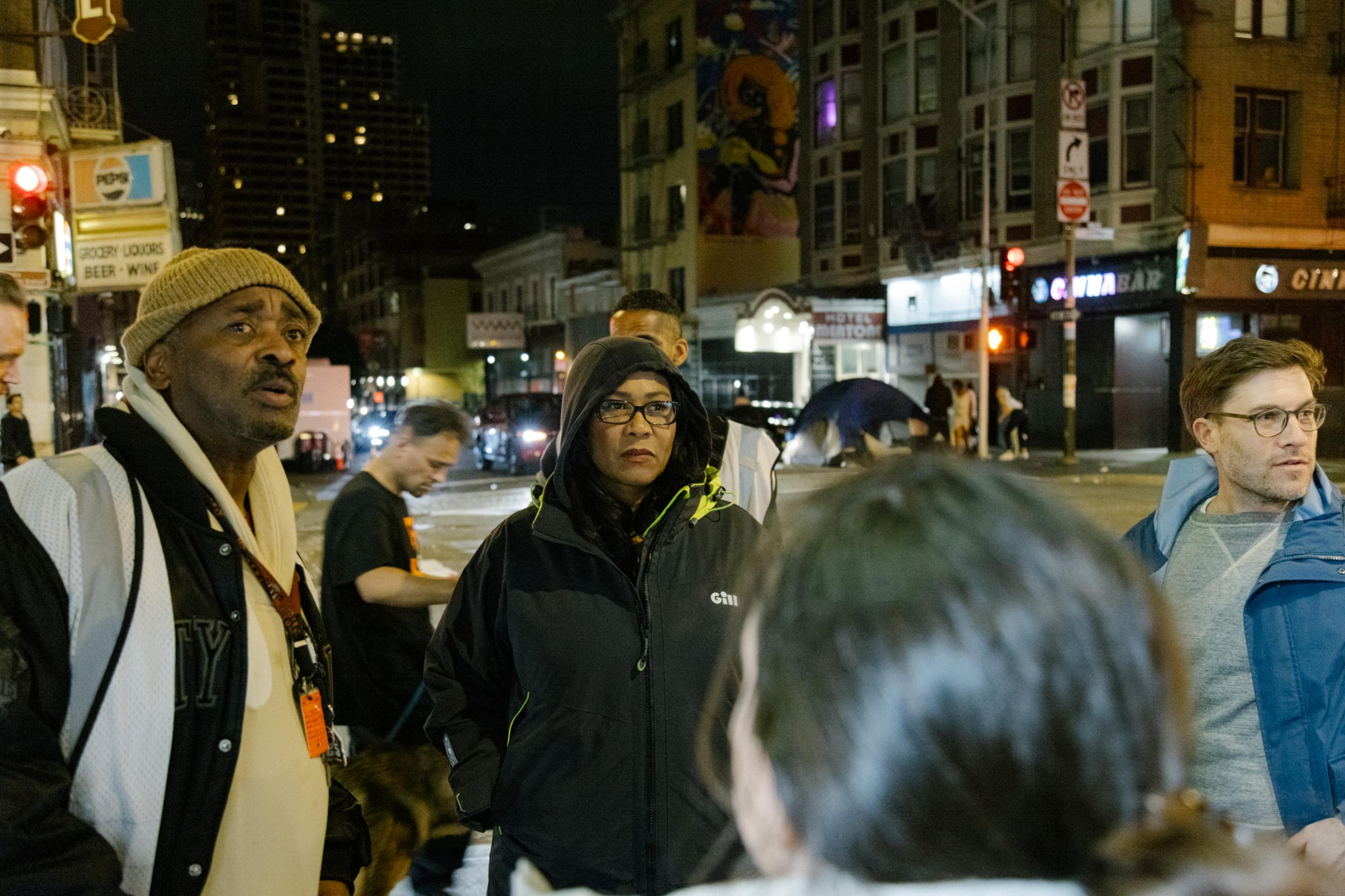 A woman stands on the sidewalk in a hoodie.